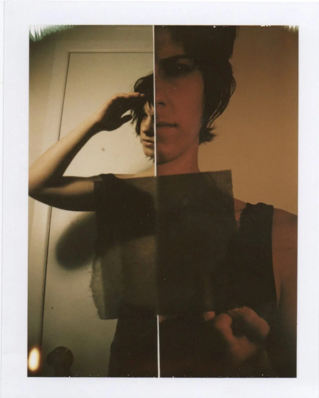 A person with dark hair and a sleeveless top taking a mirror selfie with a phone, showing a reflection with a split effect, capturing their face and upper body.