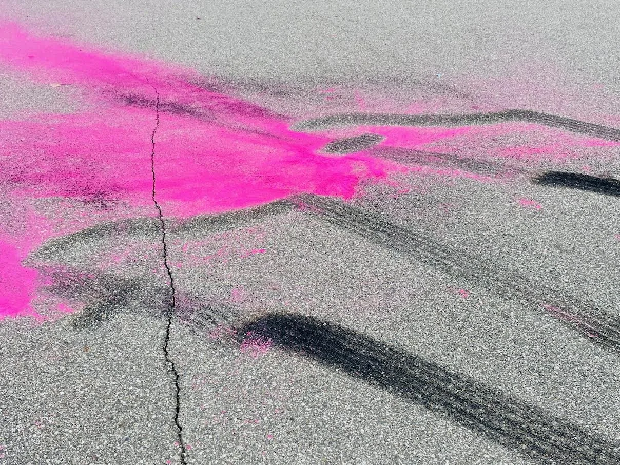 Pink spray paint on asphalt pavement with tire marks and a crack in the pavement.