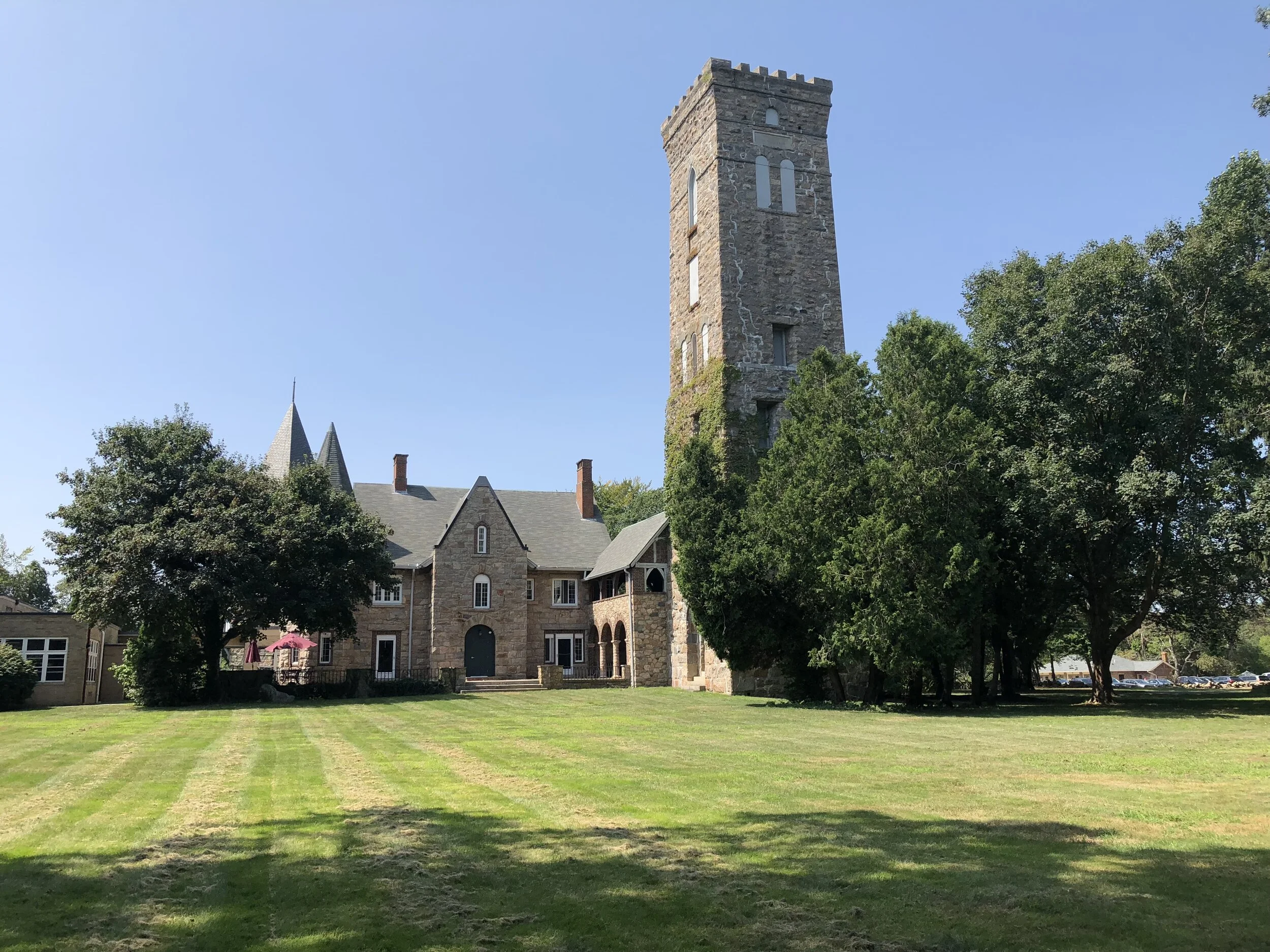 Historic stone building with a tall tower and lush green lawn under a clear blue sky.