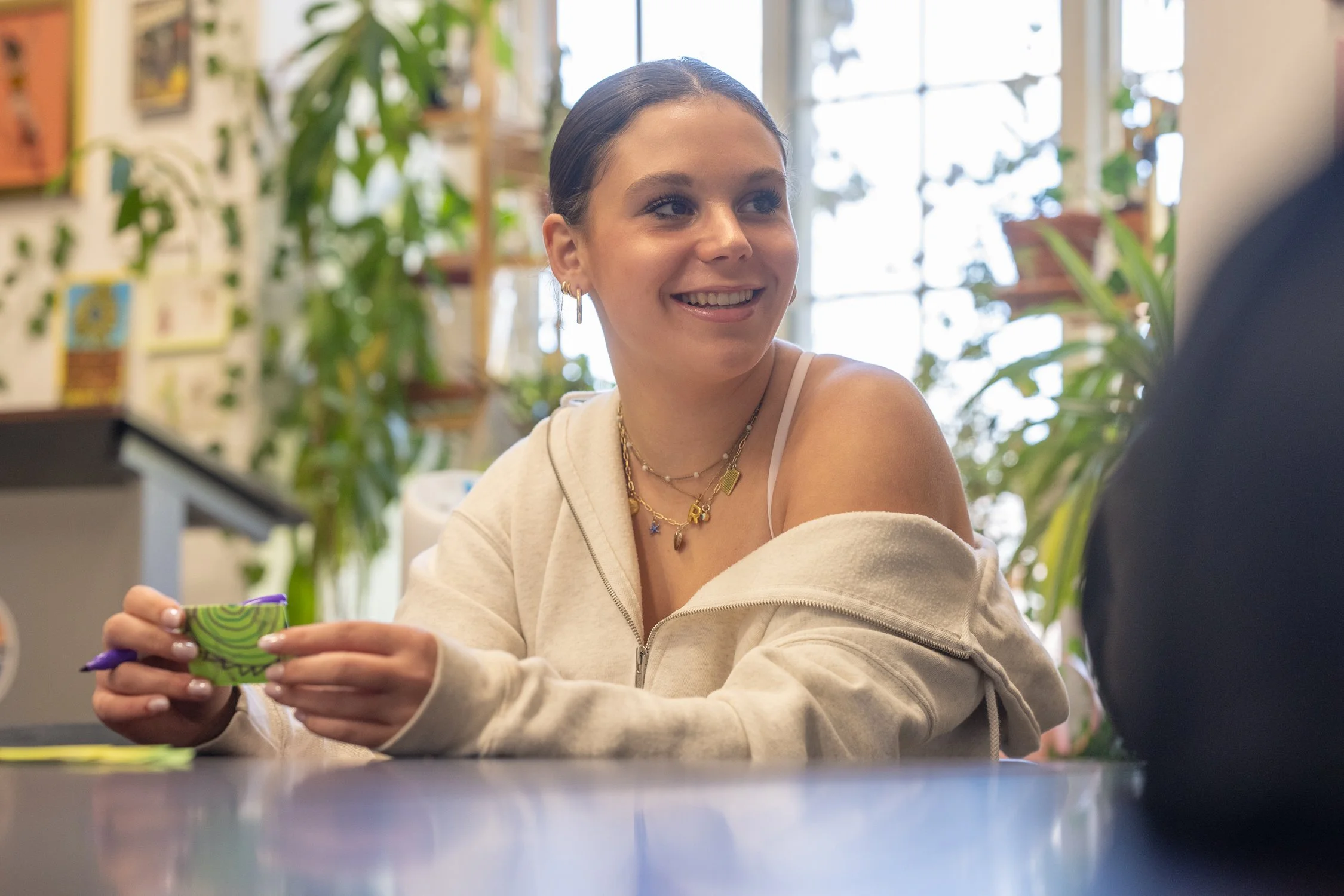 A young woman with dark hair pulled back, wearing multiple gold necklaces and hoop earrings, smiling.