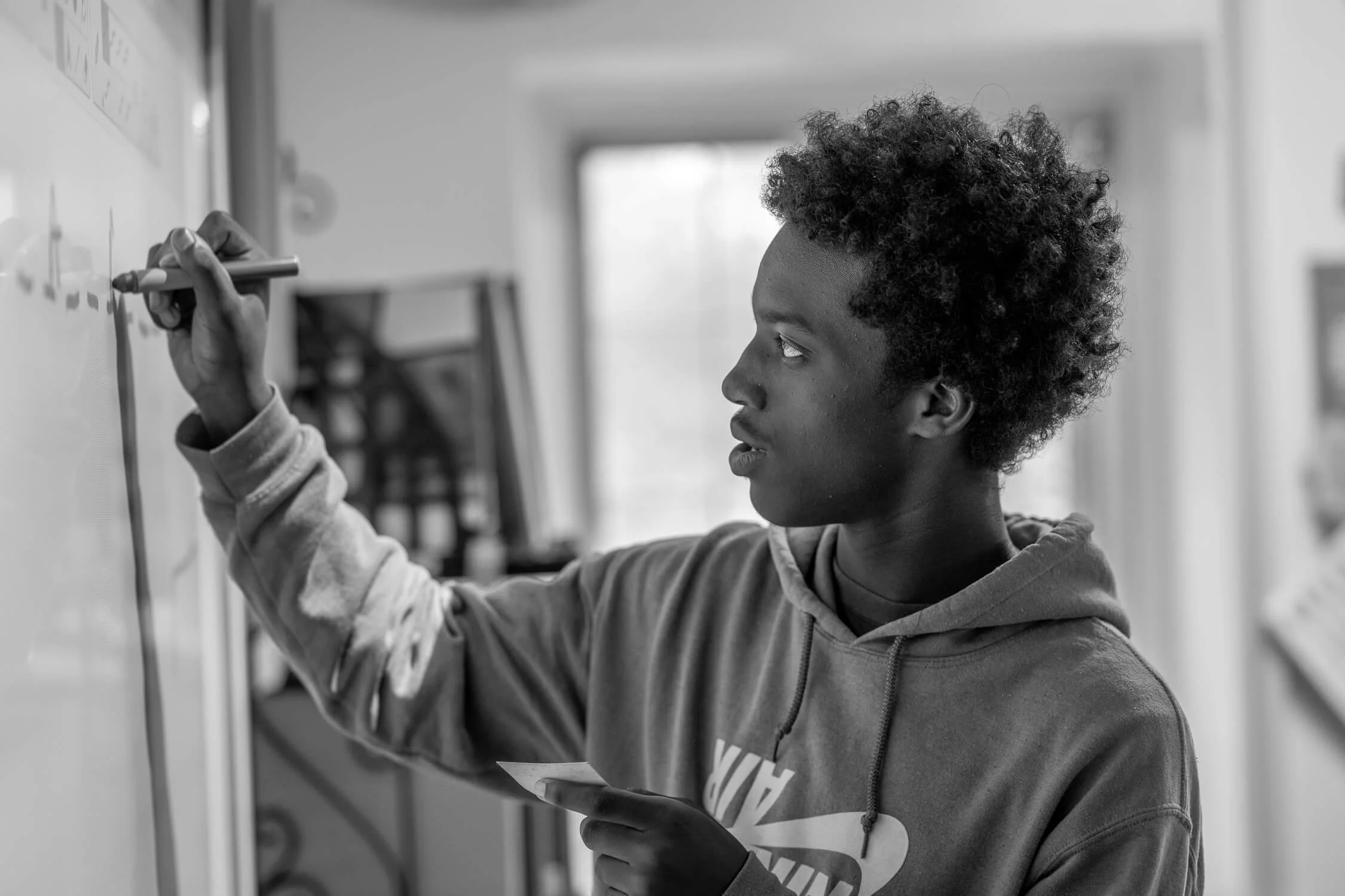 A young person writing on a whiteboard in a classroom setting.