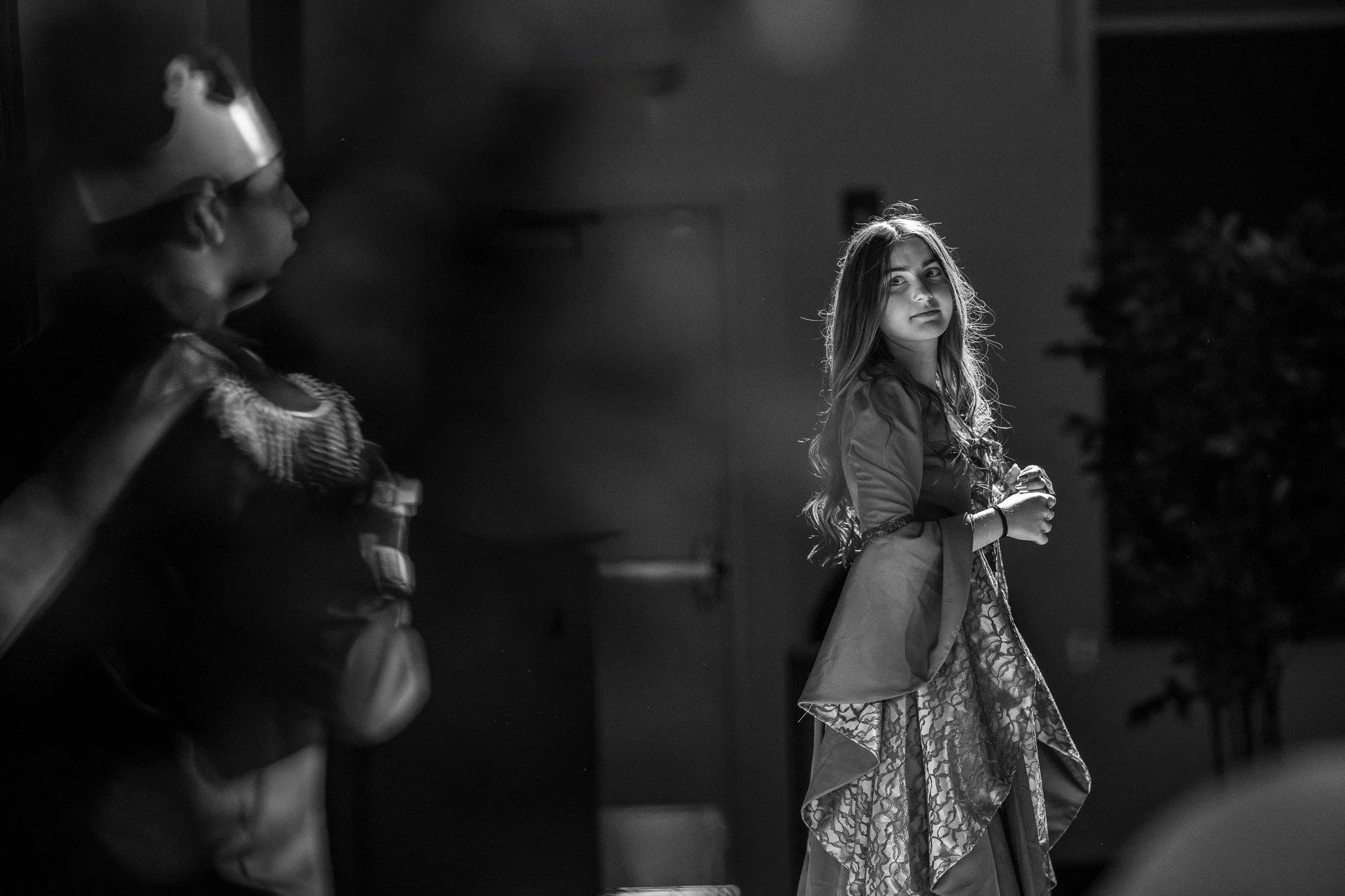 Black and white photo of a young woman in traditional attire, standing indoors with soft lighting, and another person on the left with a head covering.