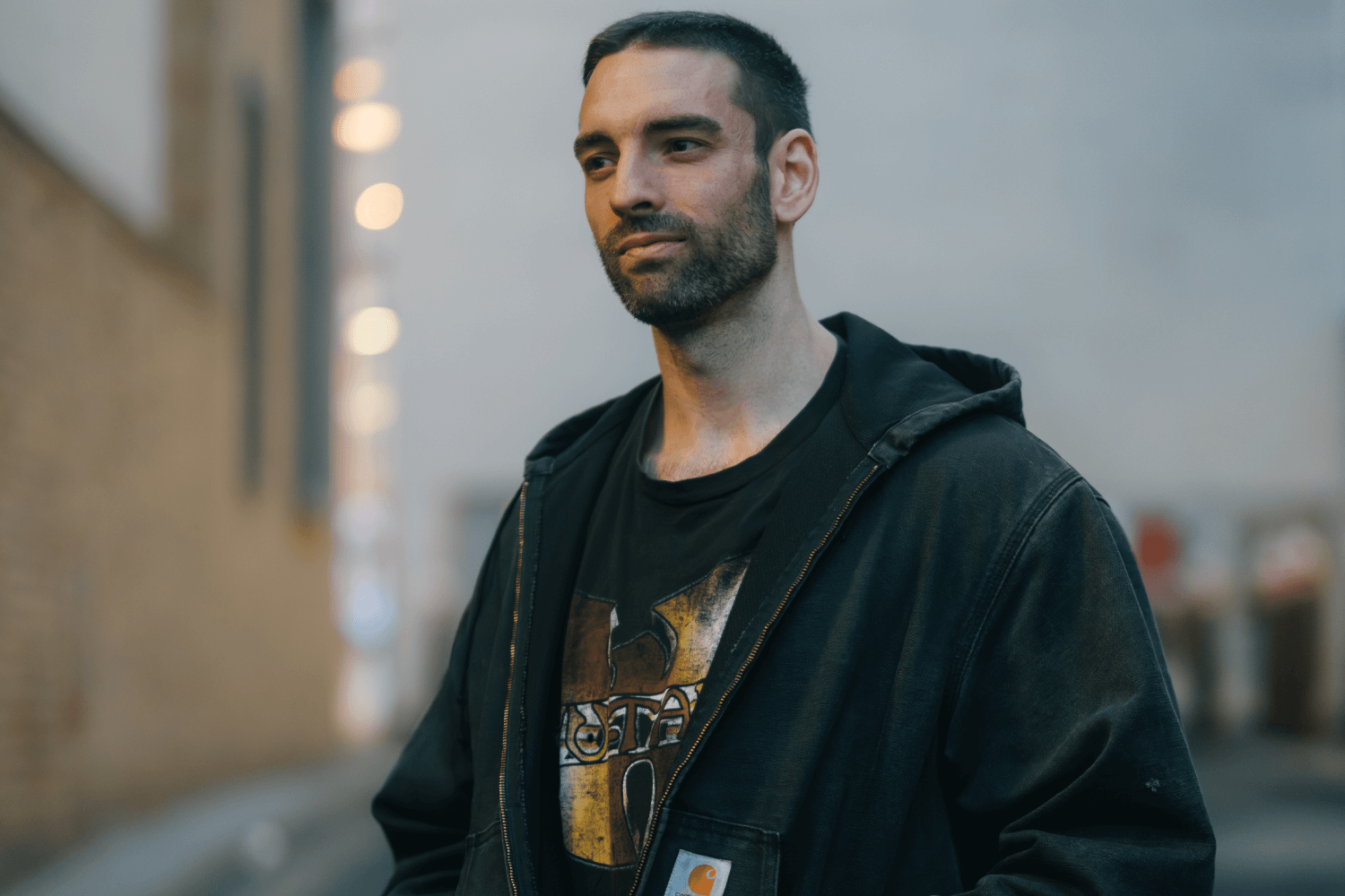 DJ Kaiyo standing in alley way wearing black carhartt jacket and black wu-tang clan t-shirt