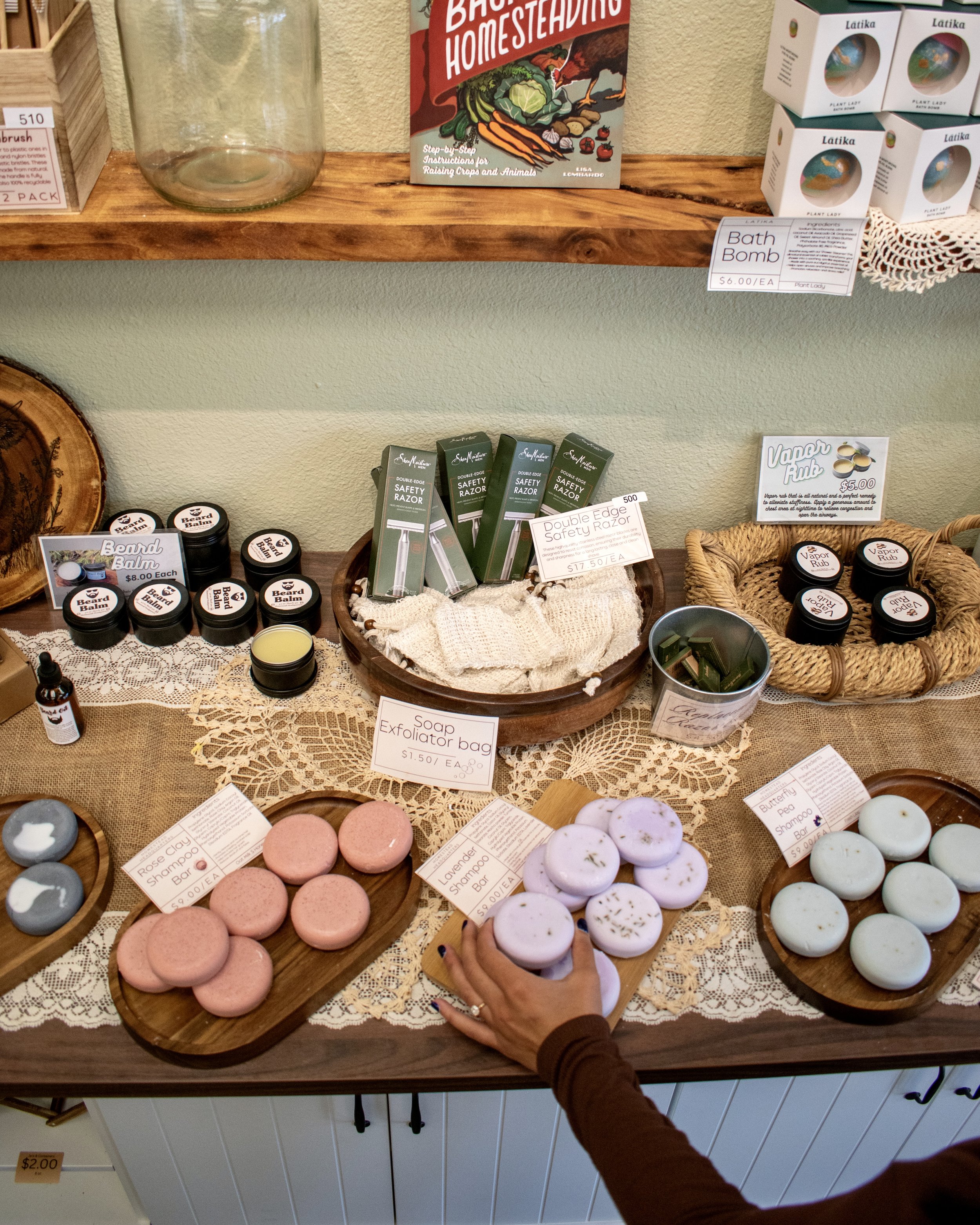 Display of bath and body products including soap, bath bombs, beard balm, safety razors, and shampoo bars at a shop.