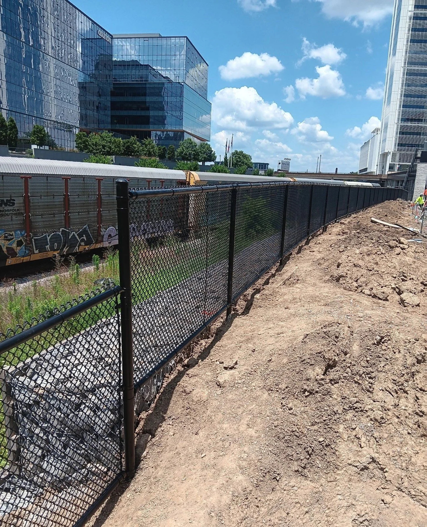 Fencing with a downtown view. 🌆 This black chain link install adds strength, security, and clean lines to an urban build. Proof that even functional projects can look sharp. 💪 Call a Kowboy today to get started on your commercial project!⁠
⁠
⁠
#Kow