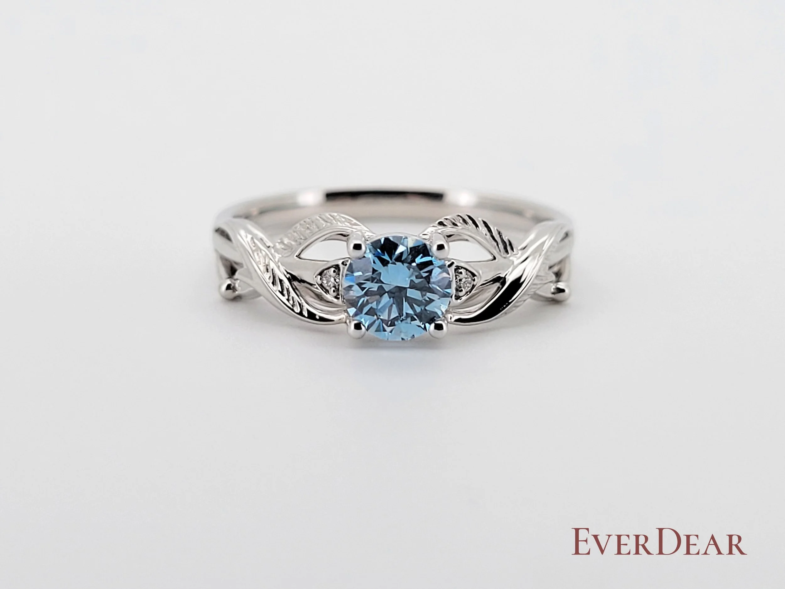 Elegant white gold or platinum ring featuring a light blue EverDear cremation diamond, adorned with intricate leaf-inspired details. A timeless piece of memorial jewelry that turns ashes or hair into diamonds, symbolizing eternal love and remembrance