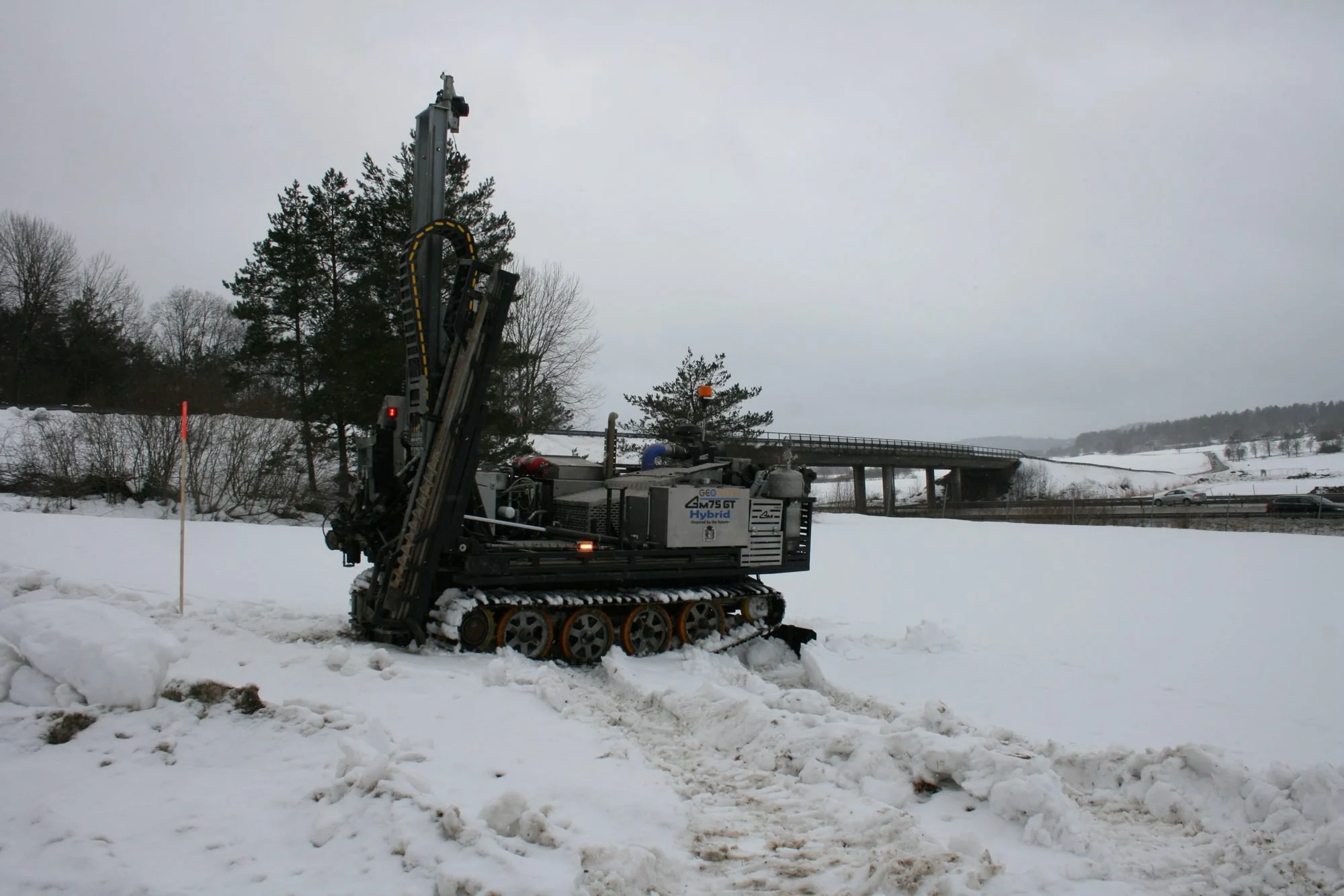Bandgående borrigg i snö nära bro och motorväg