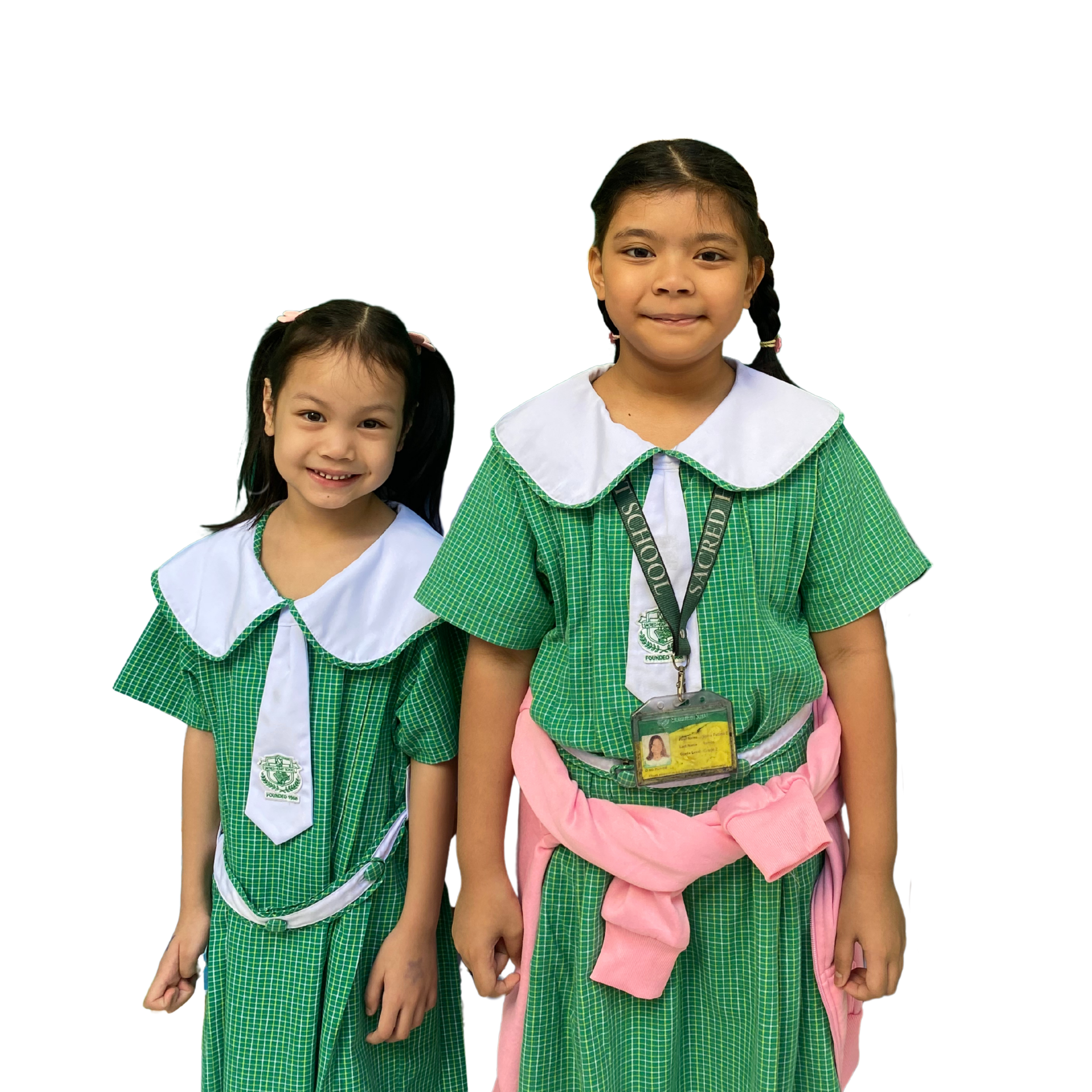 Two young girls in green plaid school uniforms with white collars and ties, smiling against a black background.
