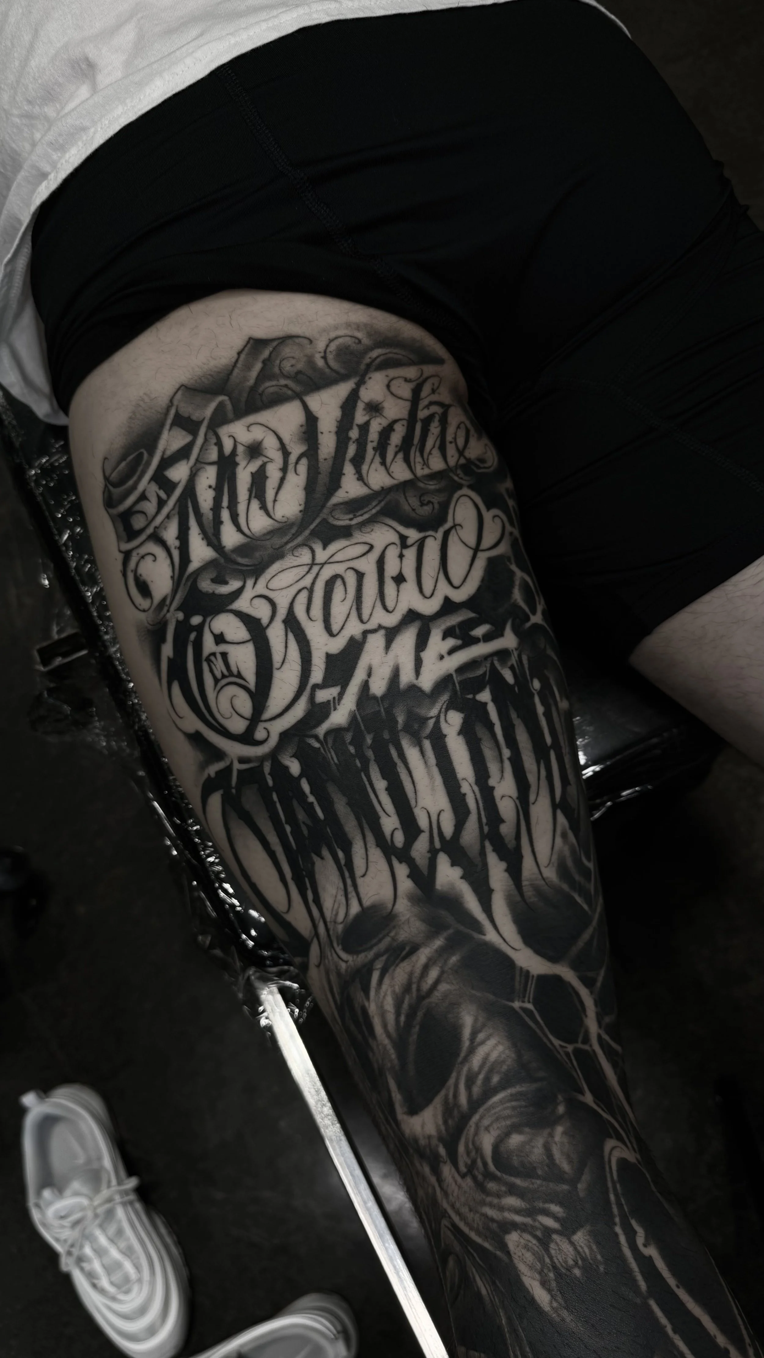 Custom blackwork leg tattoo with ornate Gothic script, dripping ink effects, and black and grey realism by The Suit of Swords.