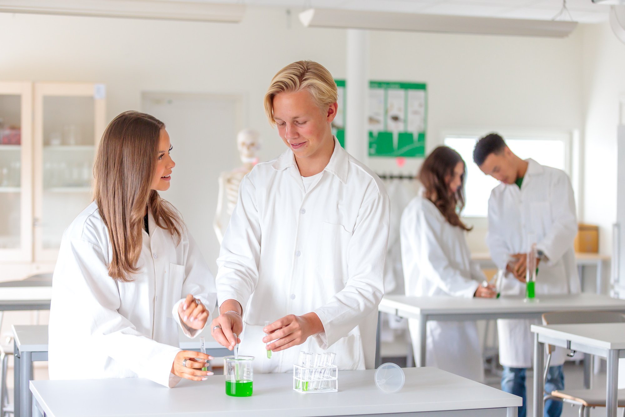 Grupp av ungdomar i labb labbrock som utför kemiexperiment i ett laboratorium