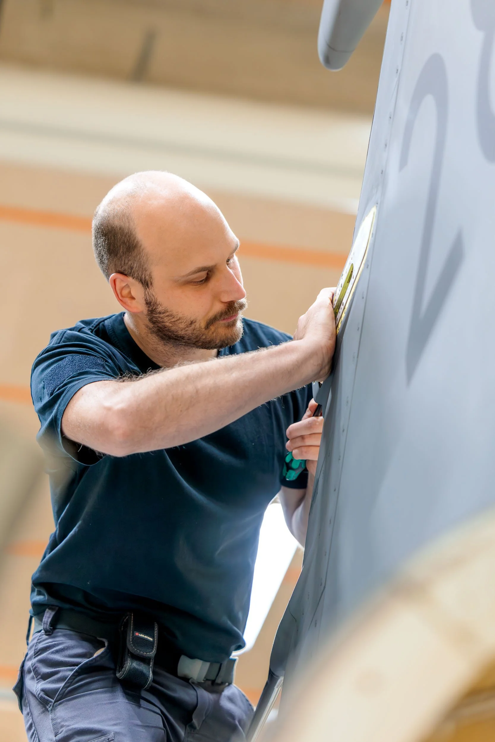 Man som arbetar med ett verktyg på en yta, eventuellt på ett flygplan eller maskin i en verkstad eller hangar.