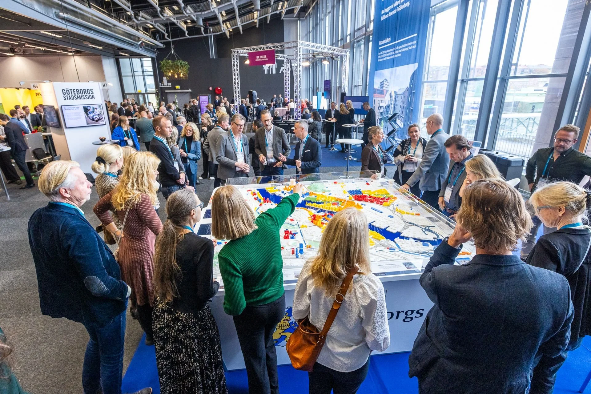 Människor samlas runt en stor LEGO-modell av Göteborgs stad i ett konferensrum.