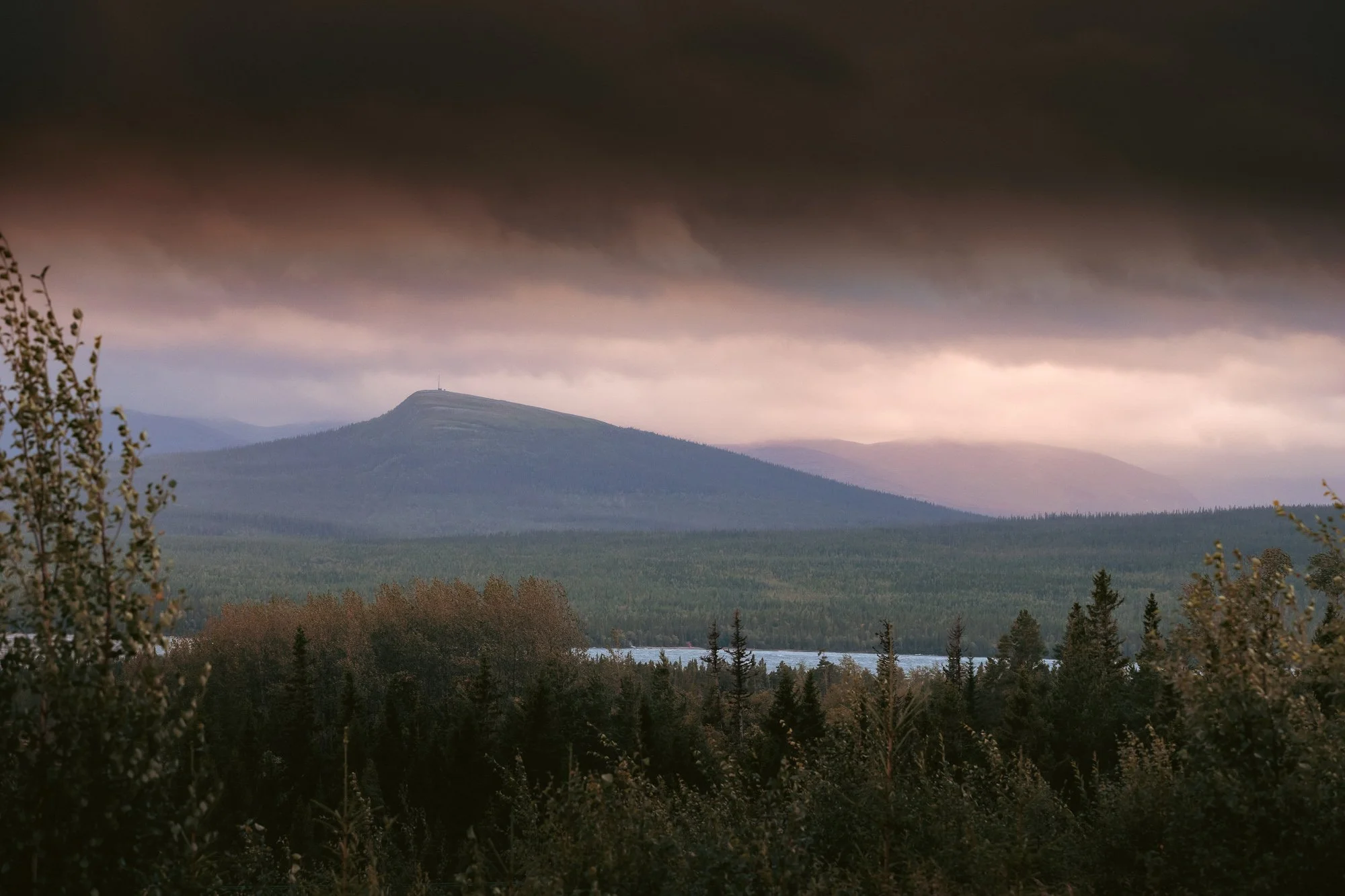 En naturskön landskapsbild med ett berg, låg molnmoln och en skog framför en sjö