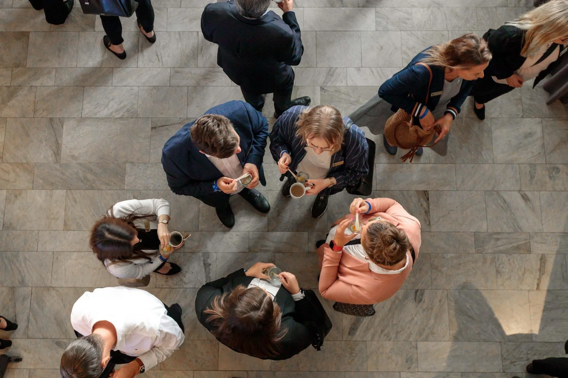 En grupp människor som dricker kaffe och står samlade på en golv av sten i ett modernt inrett utrymme.