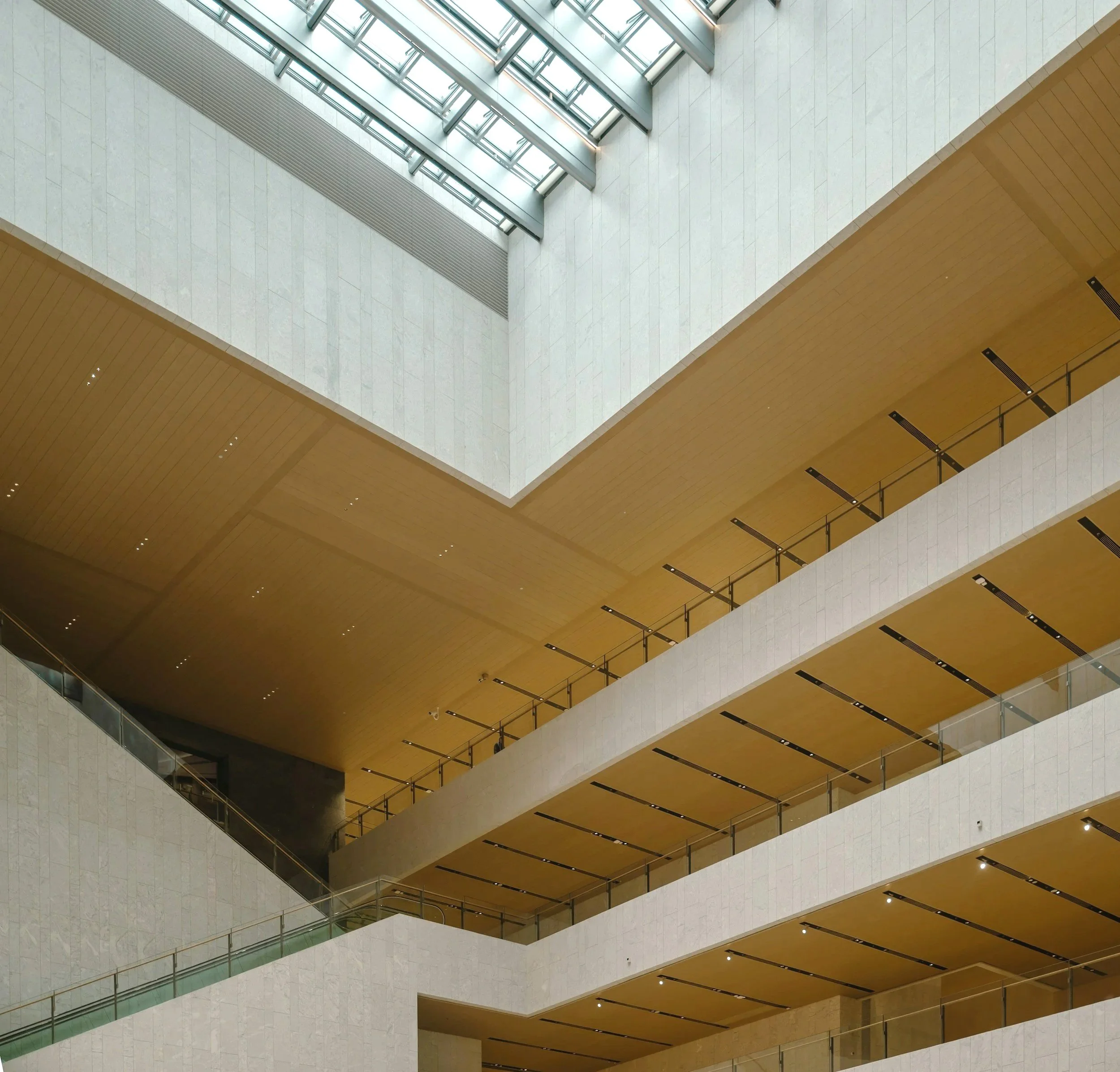 Inomhusbild av modern byggnad med flera våningar, glasfönster i taket och trappor eller promenadvägar mellan våningarna.