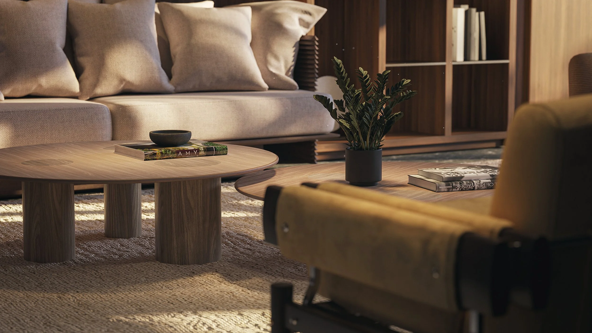 A cozy living room with a beige sofa filled with beige pillows, a round wooden coffee table with a black bowl and a magazine, a second wooden table with a potted plant and magazines, a patterned rug, and a wooden bookshelf in the background.