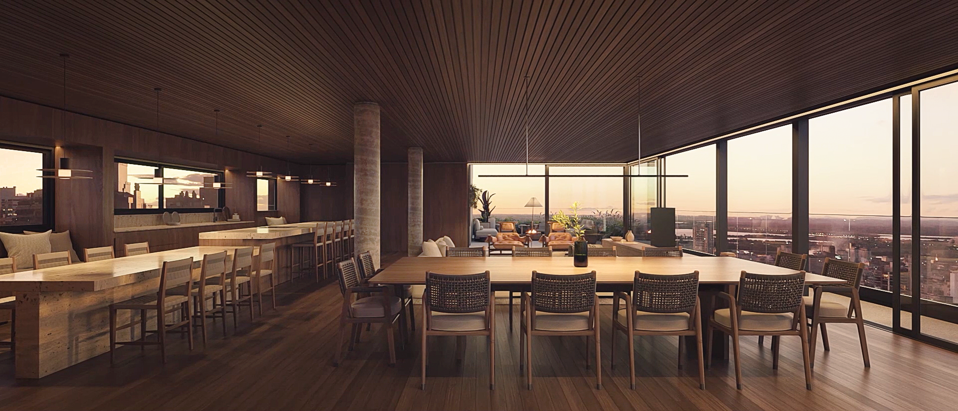 Interior of a modern high-rise apartment with a large dining table and a living area with sofas, overlooking a city skyline at sunset through floor-to-ceiling windows.