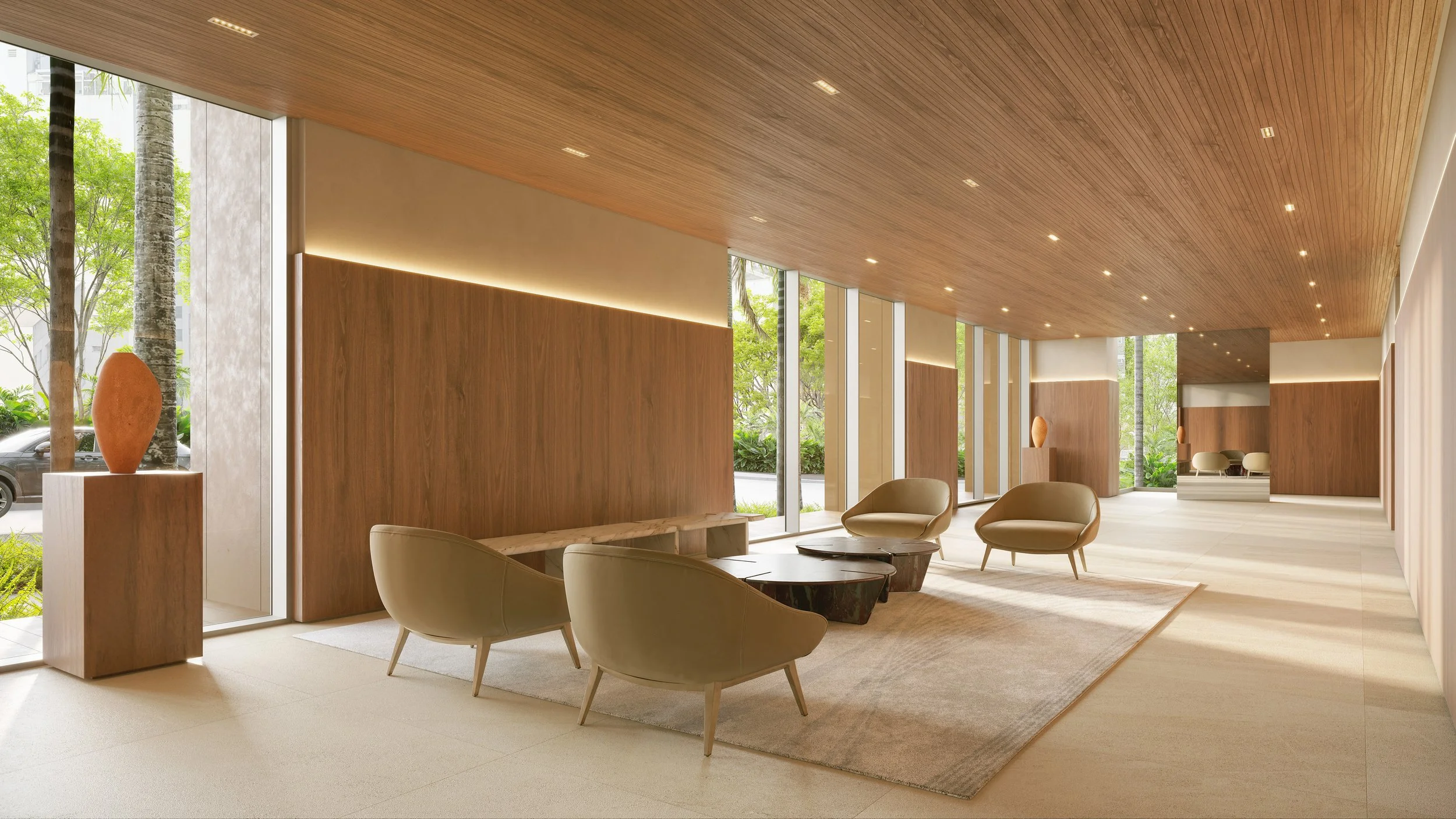 Modern hotel lobby with beige chairs, wooden accents, large glass windows showing outdoor greenery, and sculptures on pedestals.