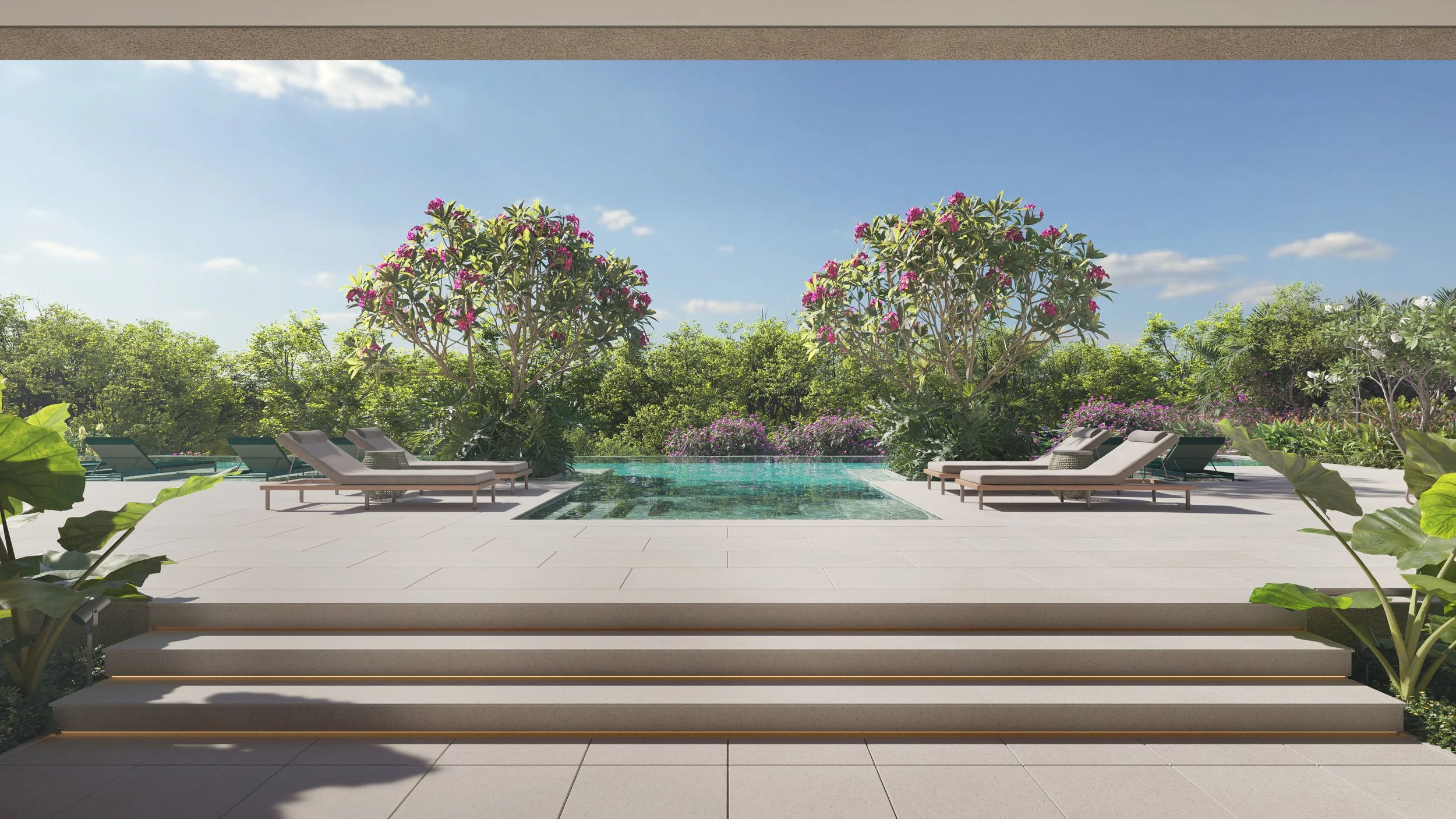View of a luxurious outdoor pool area seen through a large window, with steps leading onto a spacious patio with lounge chairs, lush green trees, colorful flowering plants, and a bright blue sky.