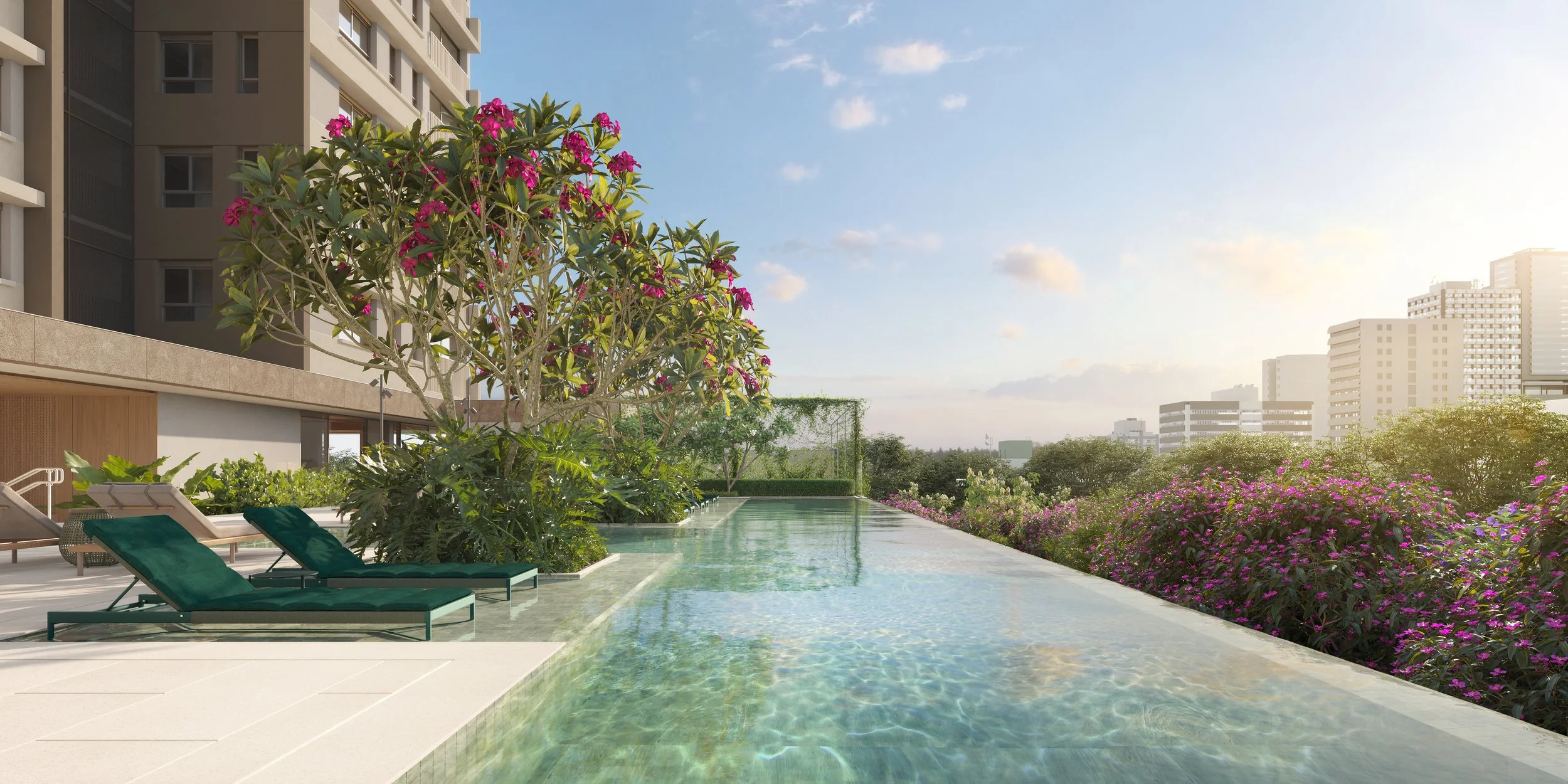 An outdoor rooftop pool area at sunset, with green lounge chairs by the pool, lush flowering plants, trees, and a city skyline in the background.