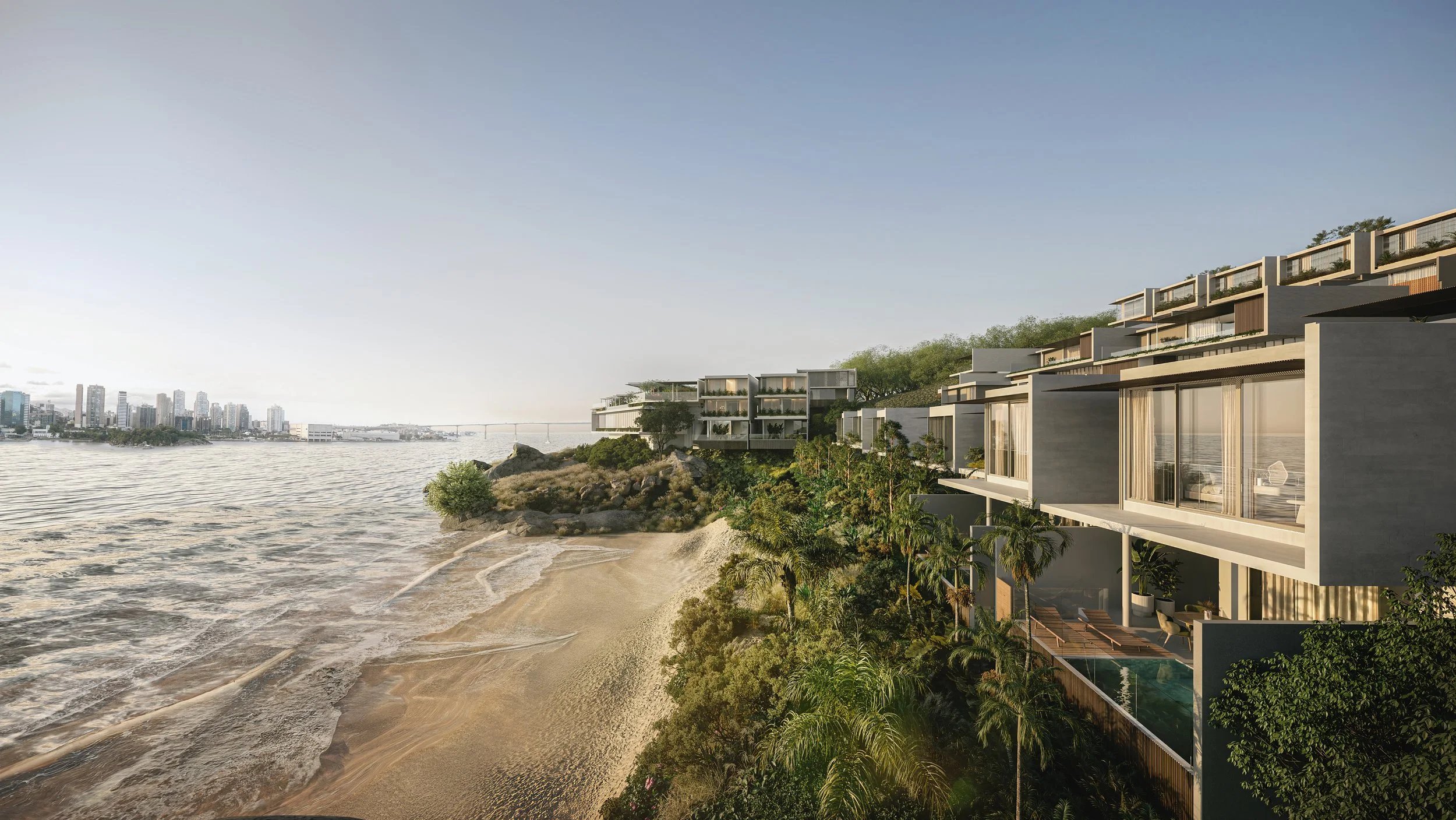 Luxury modern beachfront residences on a hillside overlooking a sandy beach and water with a city skyline in the distance during sunset.