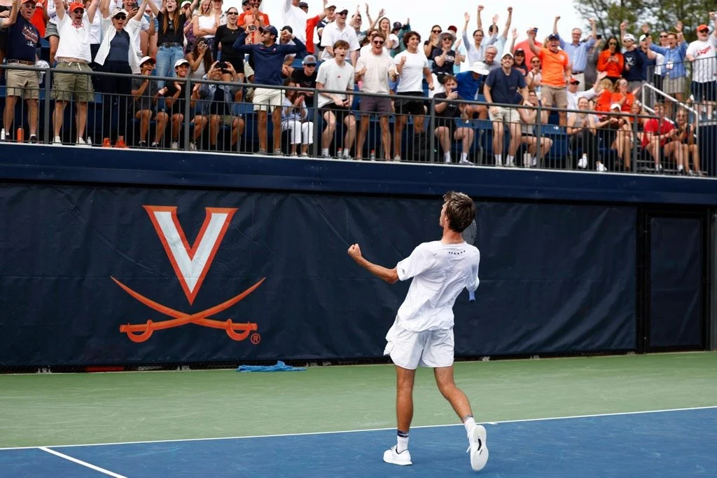 Dylan Dietrich auf dem Platz, feiert einen Sieg vor einem jubelnden Publikum mit den Armen in die Luft. Das Logo der University of Virginia ist im Hintergrund sichtbar.