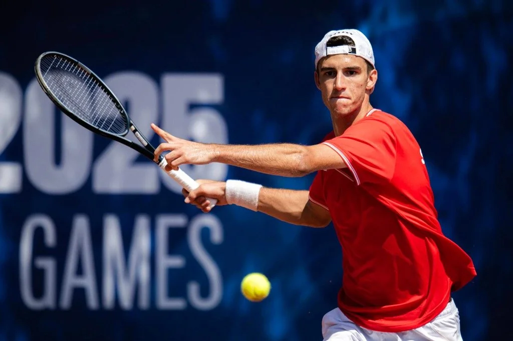 Dylan Dietrich spielt Tennis bei den 2022 NCAA-Spielen, trägt rotes T-Shirt und weiße Kappe, schwingt Tennisschläger, auf Tennisplatz.