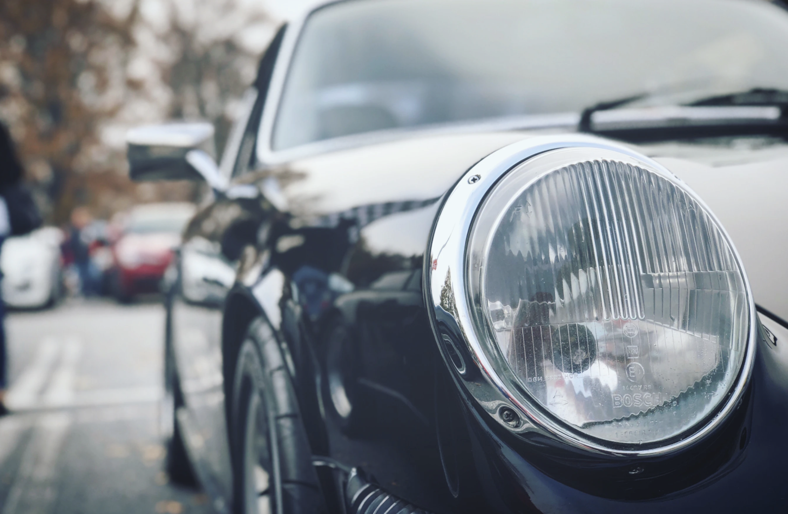 Close-up of a classic car's headlight and front fender, showing chrome detailing and part of the tire.