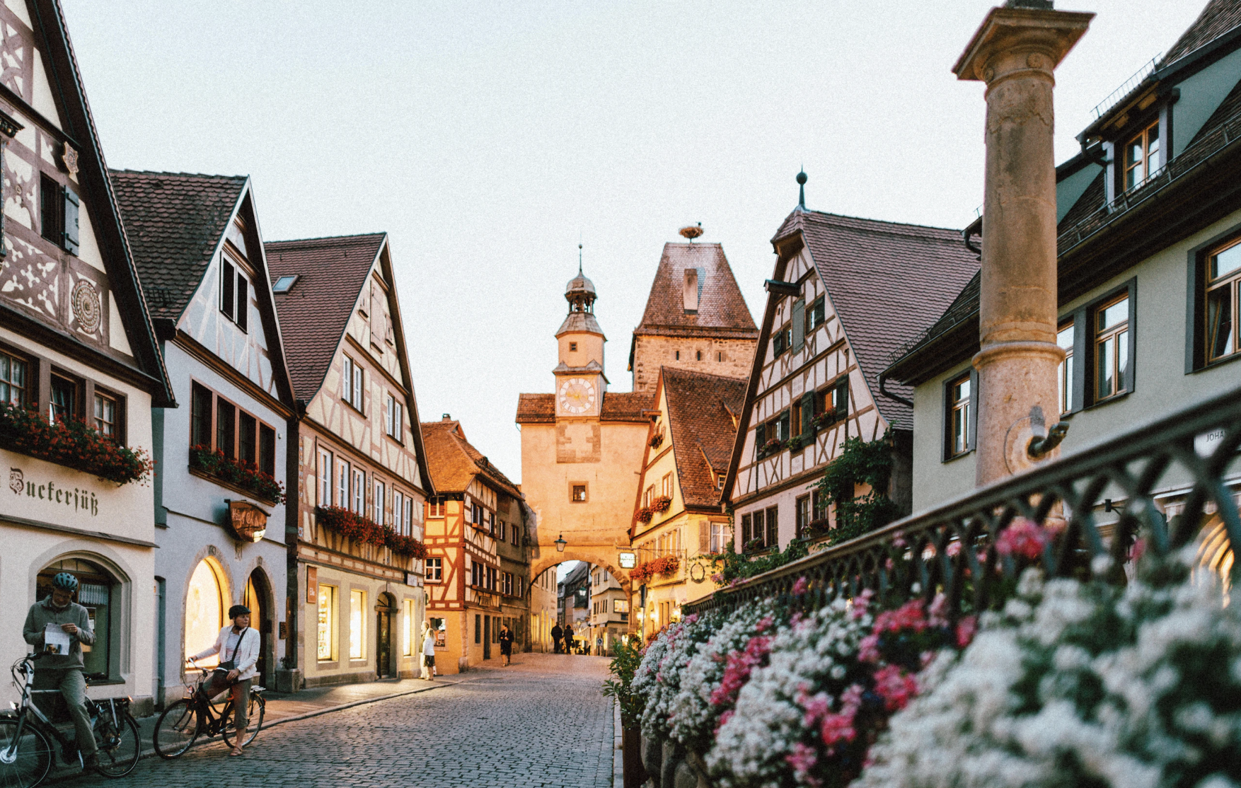 Quaint European street with half-timbered houses in Rothenburg ob der Tauber at sunset, featuring cobblestone pavement and floral decorations.