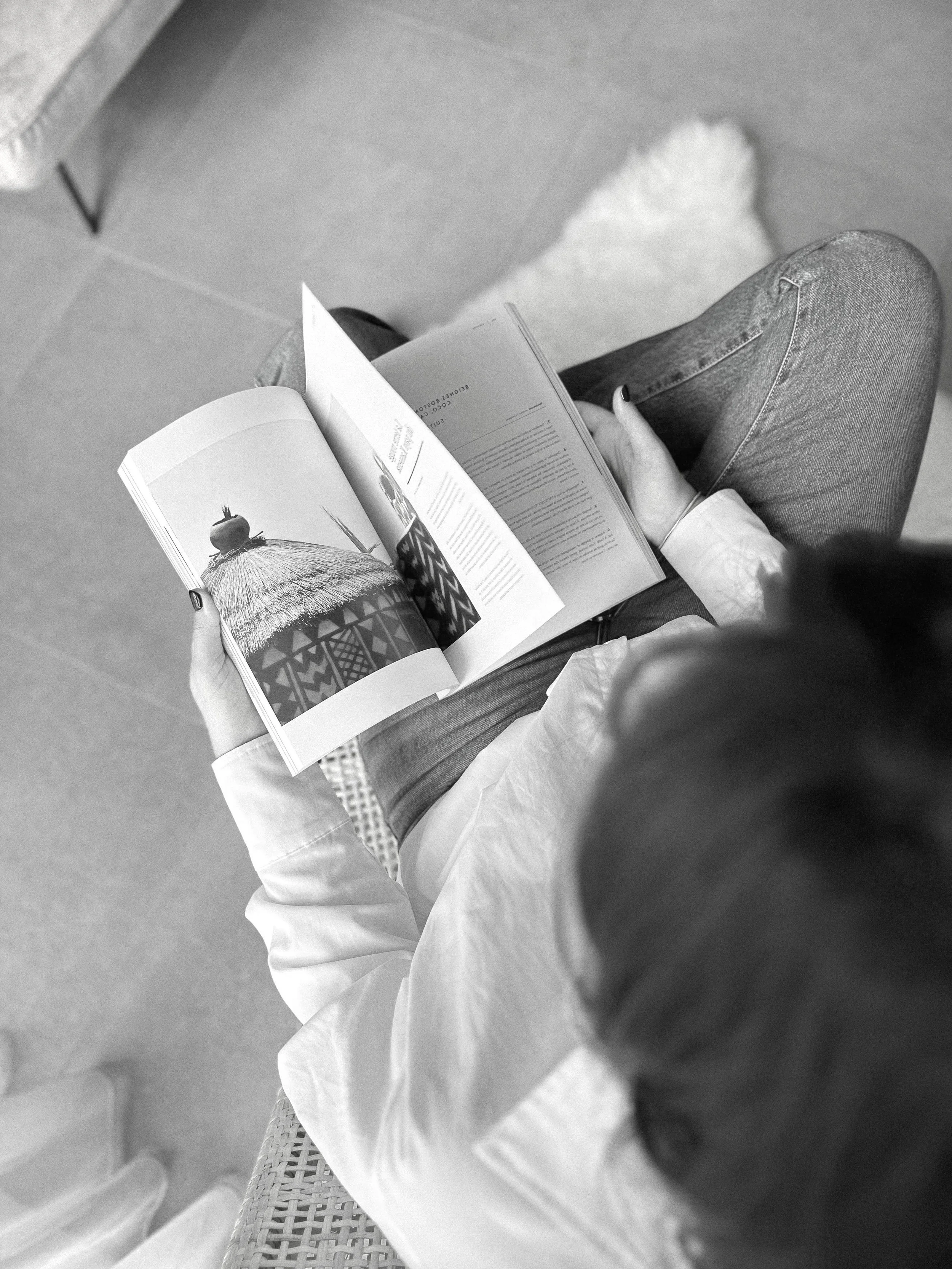 Personne lisant un livre illustré, vu de haut, en noir et blanc.