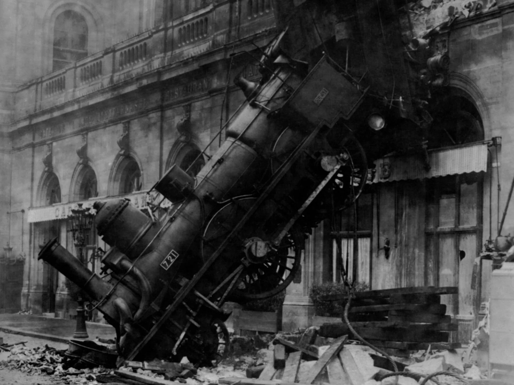 A vintage steam train derailment crash on a city street with damaged tracks and debris.