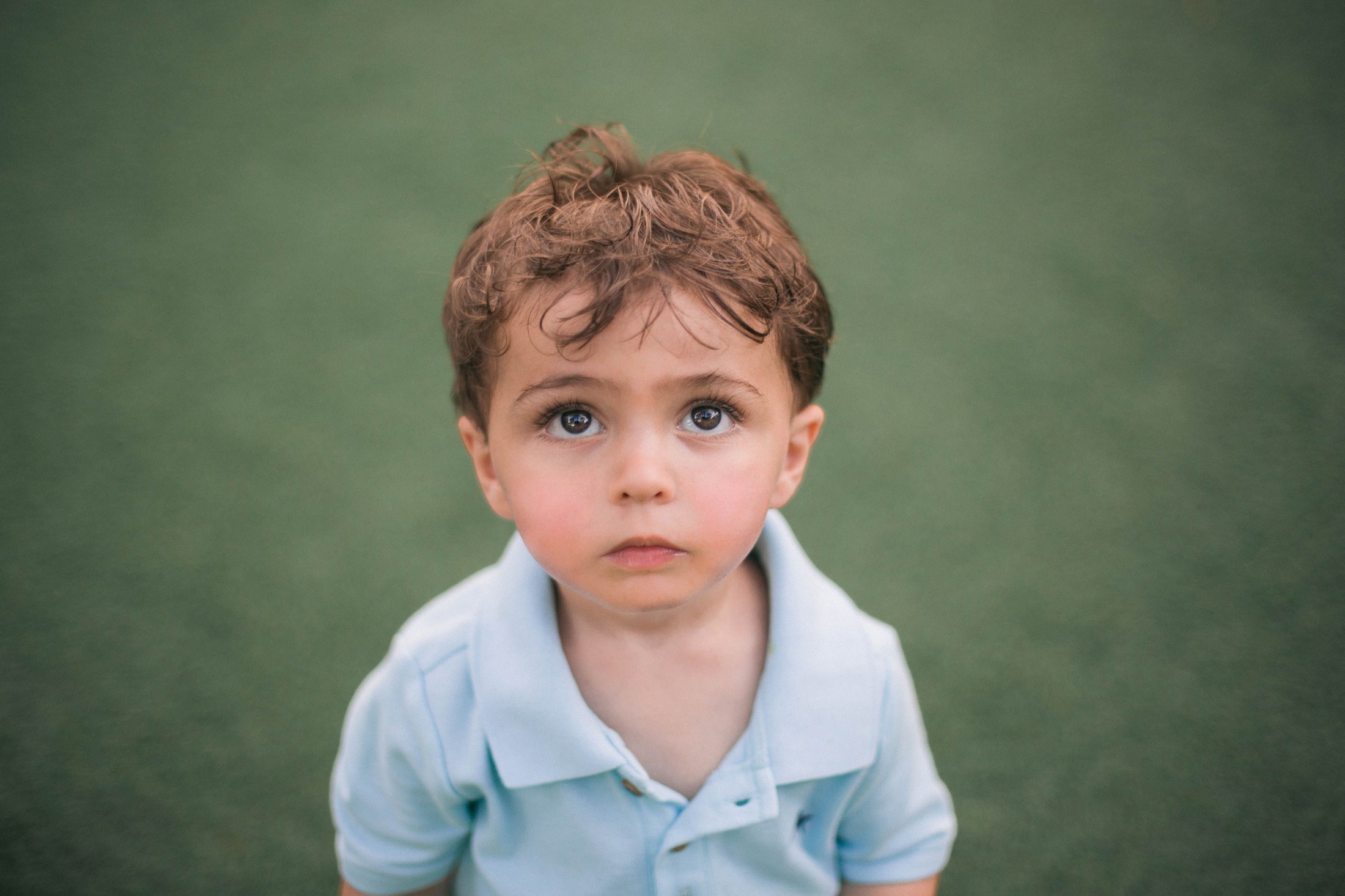 A young child with brown hair looking upward innocently at their hero parent