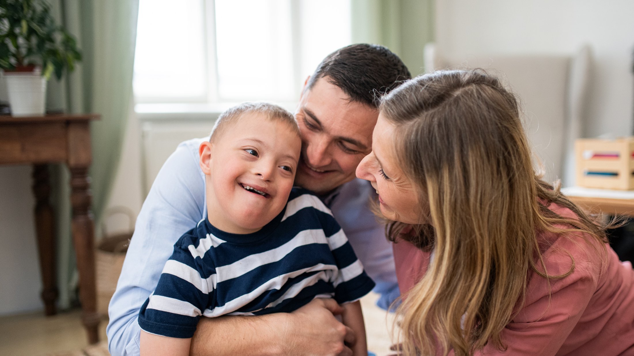 A happy young boy with Down syndrome in a red striped shirt, smiling warmly to camera keep him safe by using Protect Our Family
