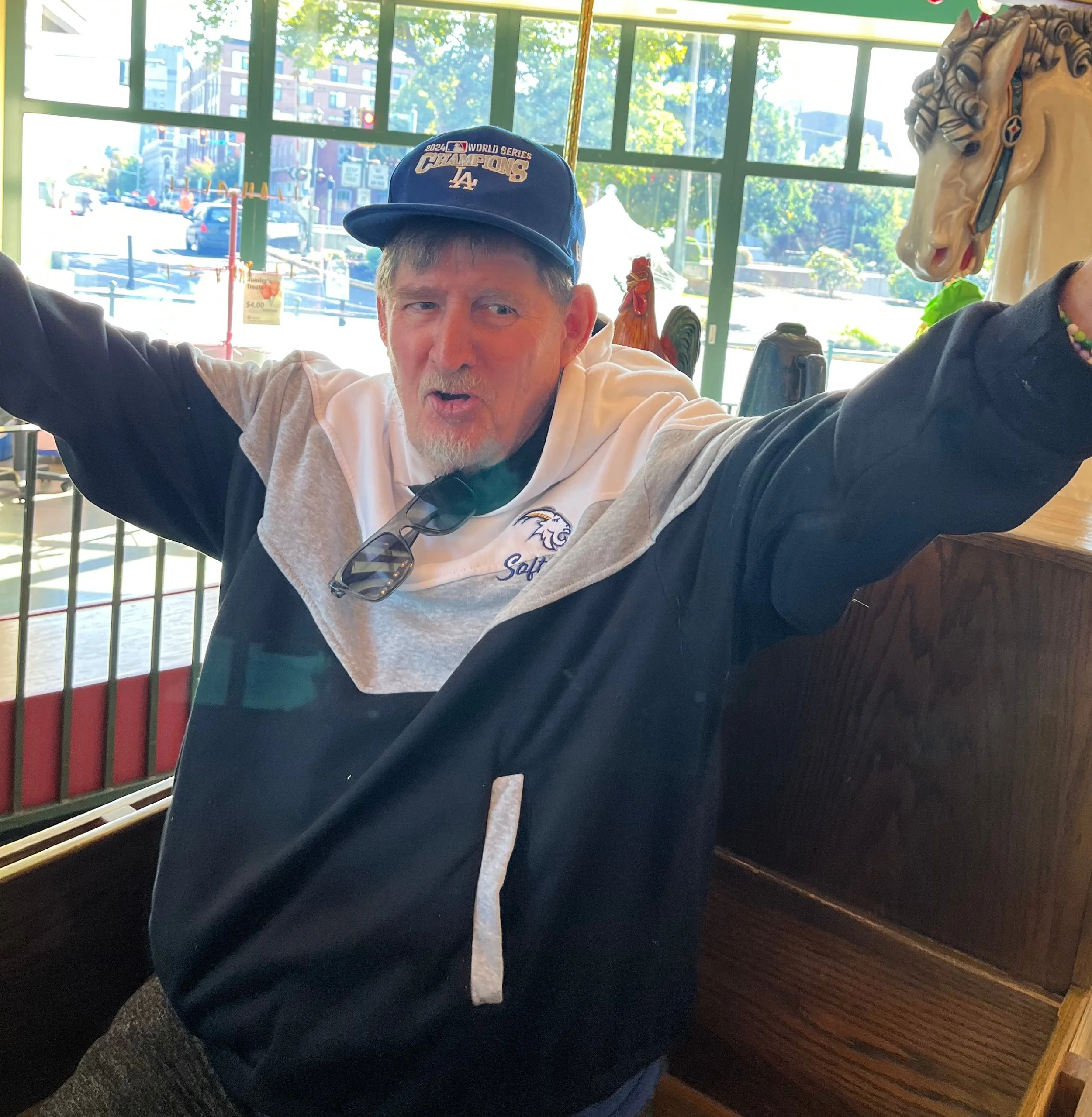 Portrait of a man with gray hair and beard wearing a maroon sweater, standing indoors near a window.