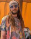 A man with long hair and a beard sitting in a room with a white door behind him.
