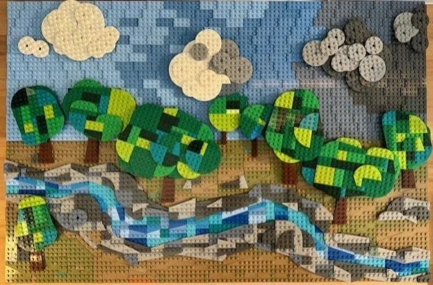 Lego mosaic of a landscape with a river, trees, mountains, and clouds.