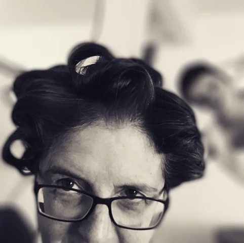 Black and white photo of a woman with dark hair and glasses, with a background featuring a blurred person.