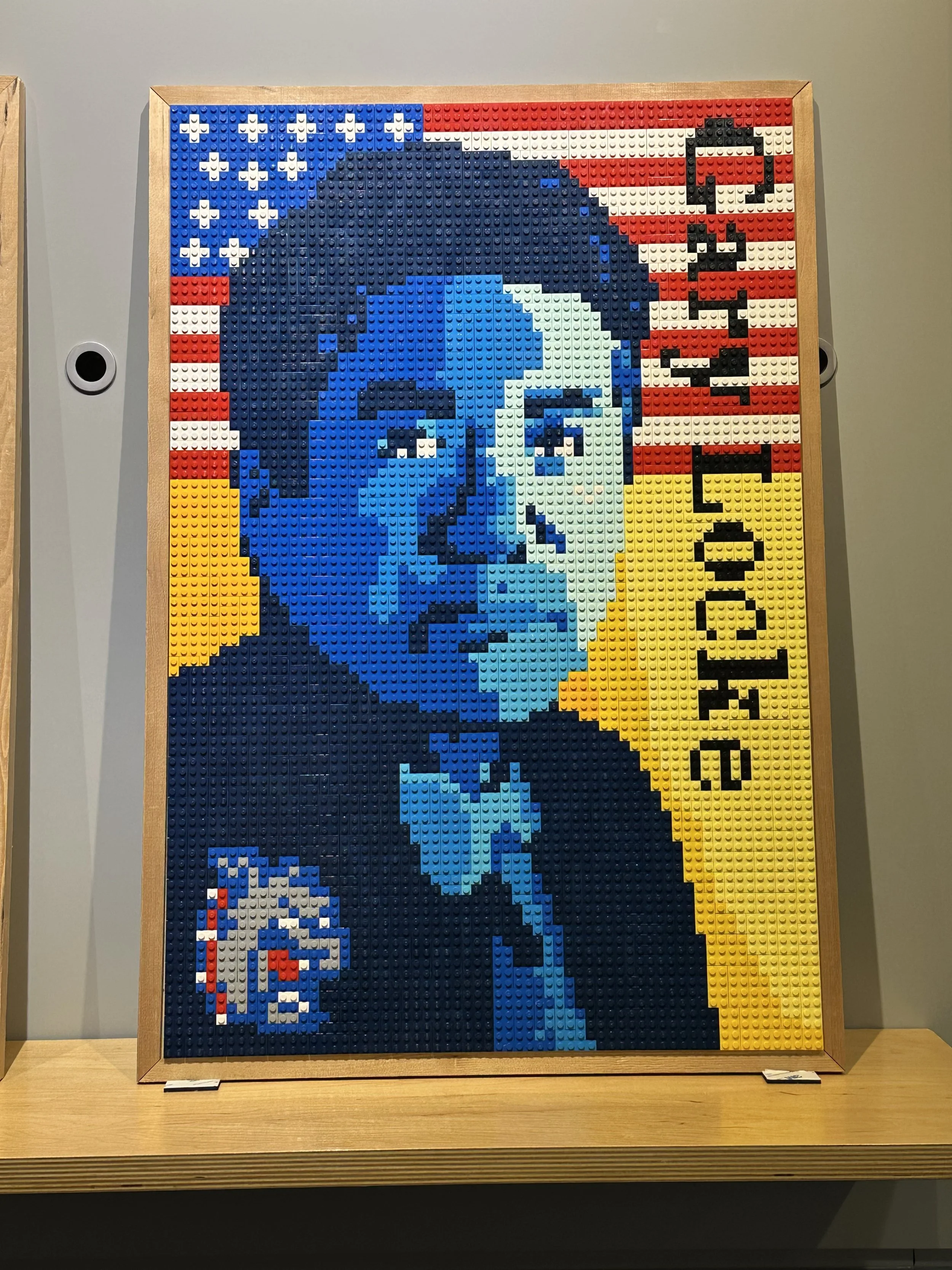 Lego mosaic of a man in glasses and bow tie with American flag background and