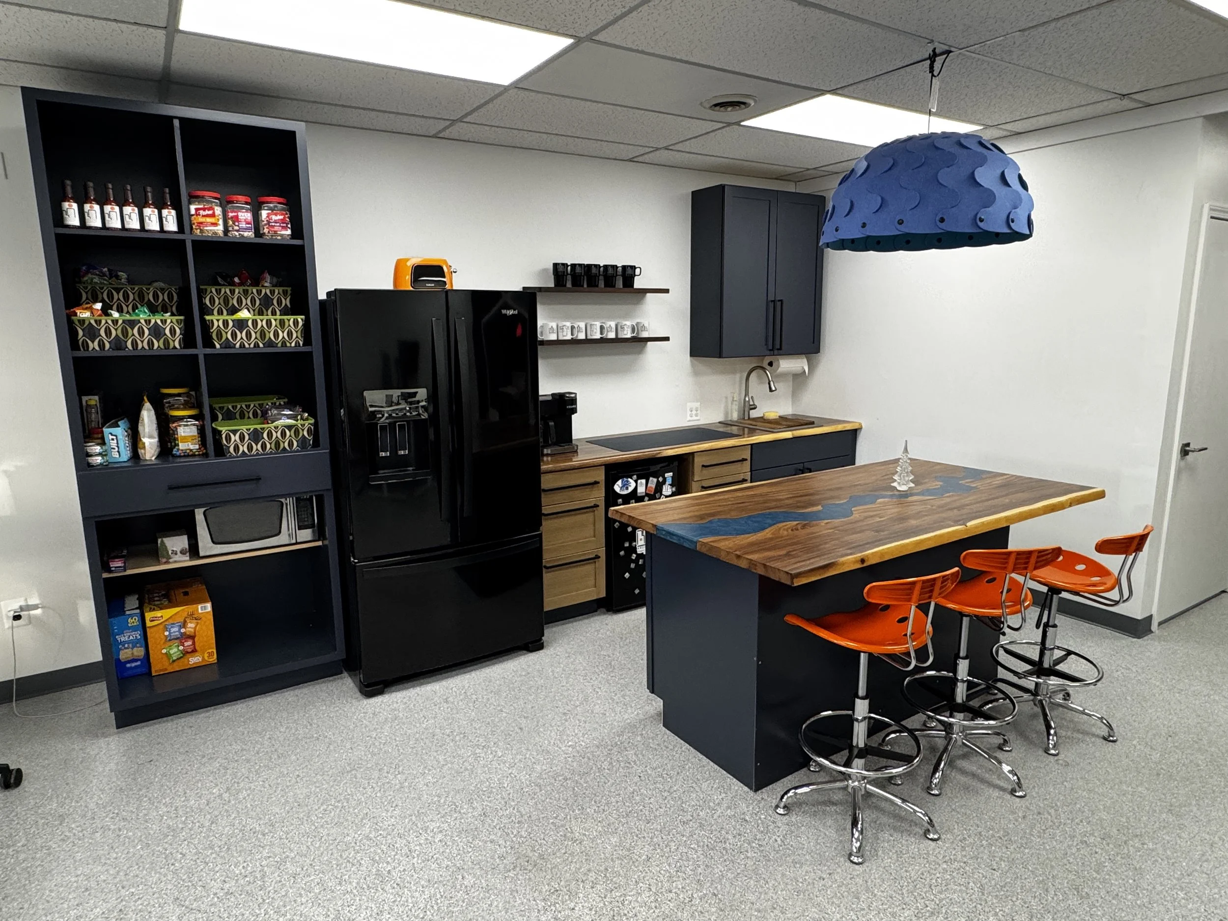 Modern kitchen with black appliances, wooden countertops, and orange barstools. A blue hanging light fixture and a small decorative Christmas tree are also visible.