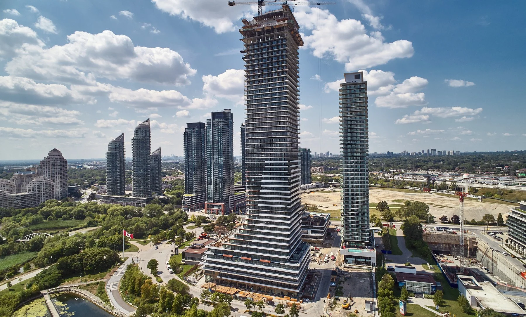 High-rise buildings under construction in an urban area, with cranes, surrounded by greenery and blue sky with clouds.