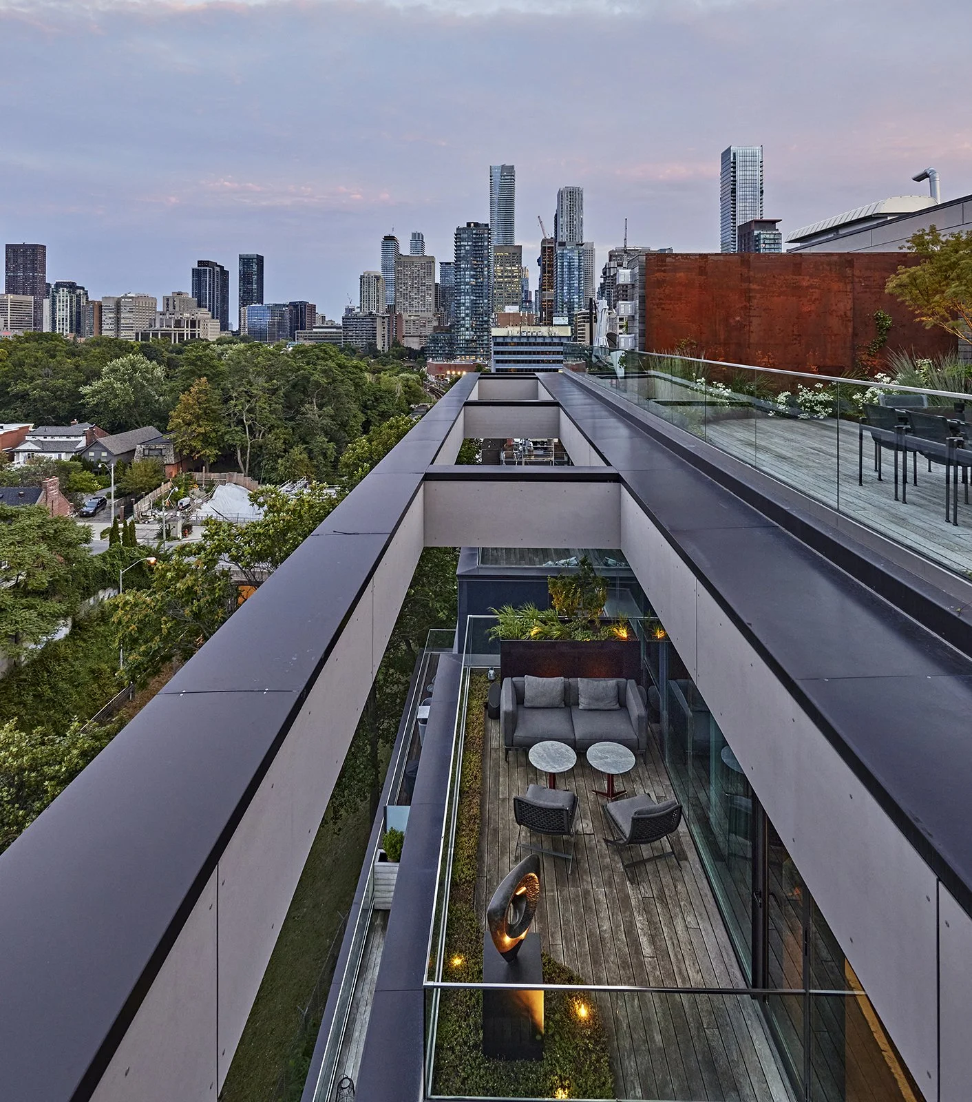 View of a modern rooftop terrace with seating area and city skyline in the background during dusk.