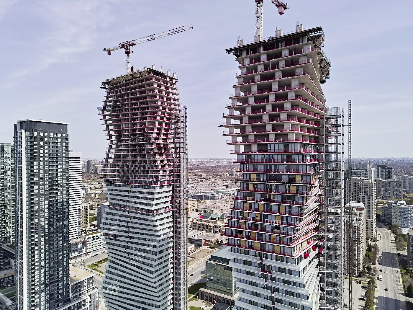 Two high-rise buildings under construction in an urban area with cranes on top.