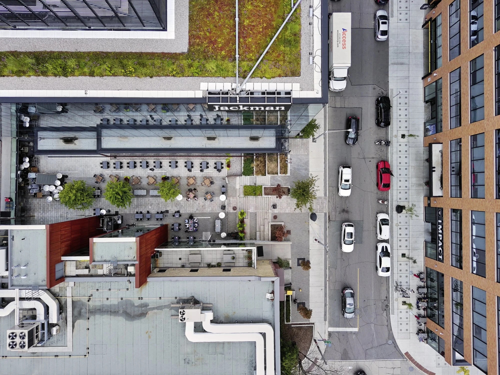 Urban street view with parked cars, sidewalk cafes, and modern office buildings surrounded by greenery.