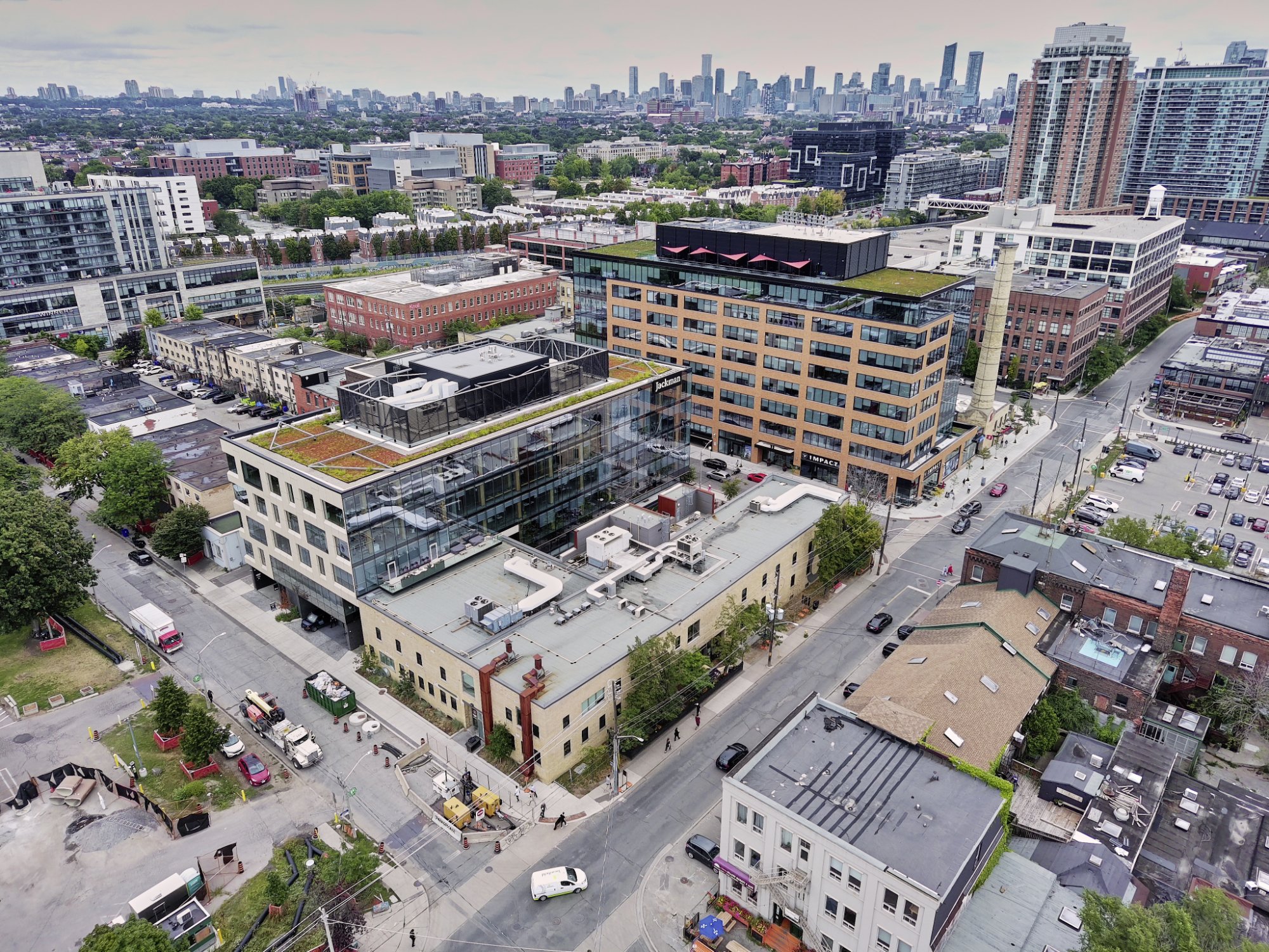 Aerial view of a cityscape showing a mix of modern and older buildings, streets, parking lots, and skyscrapers in the background.