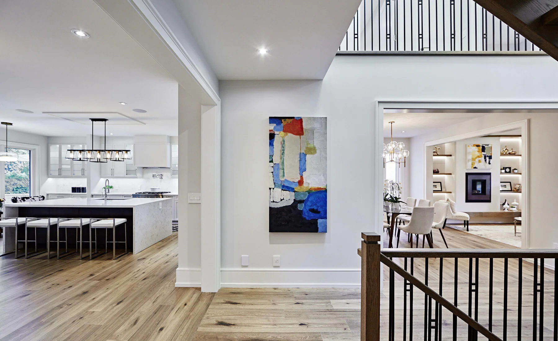 Open-concept interior of a modern home showing a kitchen with an island, dining area, and living room in the background, with hardwood flooring and contemporary decor.