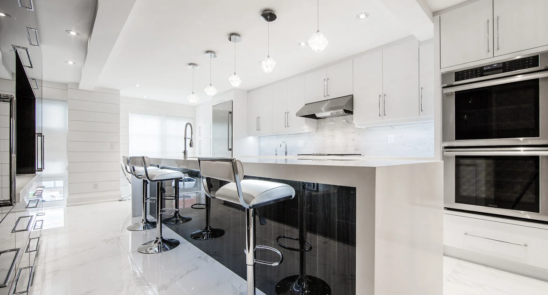 Modern kitchen with white cabinets, marble island, bar stools, stainless steel appliances, and pendant lighting.