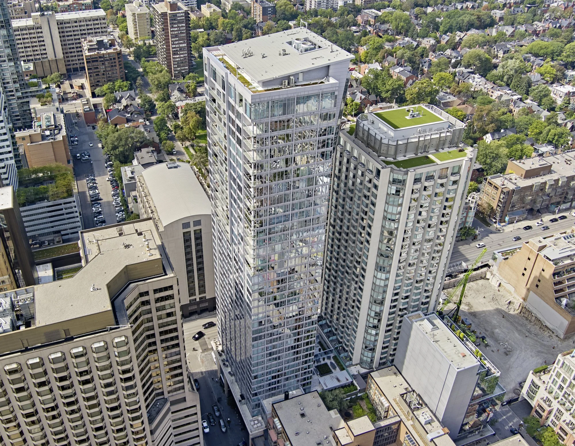 Aerial view of a city with tall modern glass and concrete skyscrapers, surrounding smaller older buildings, and street traffic visible.