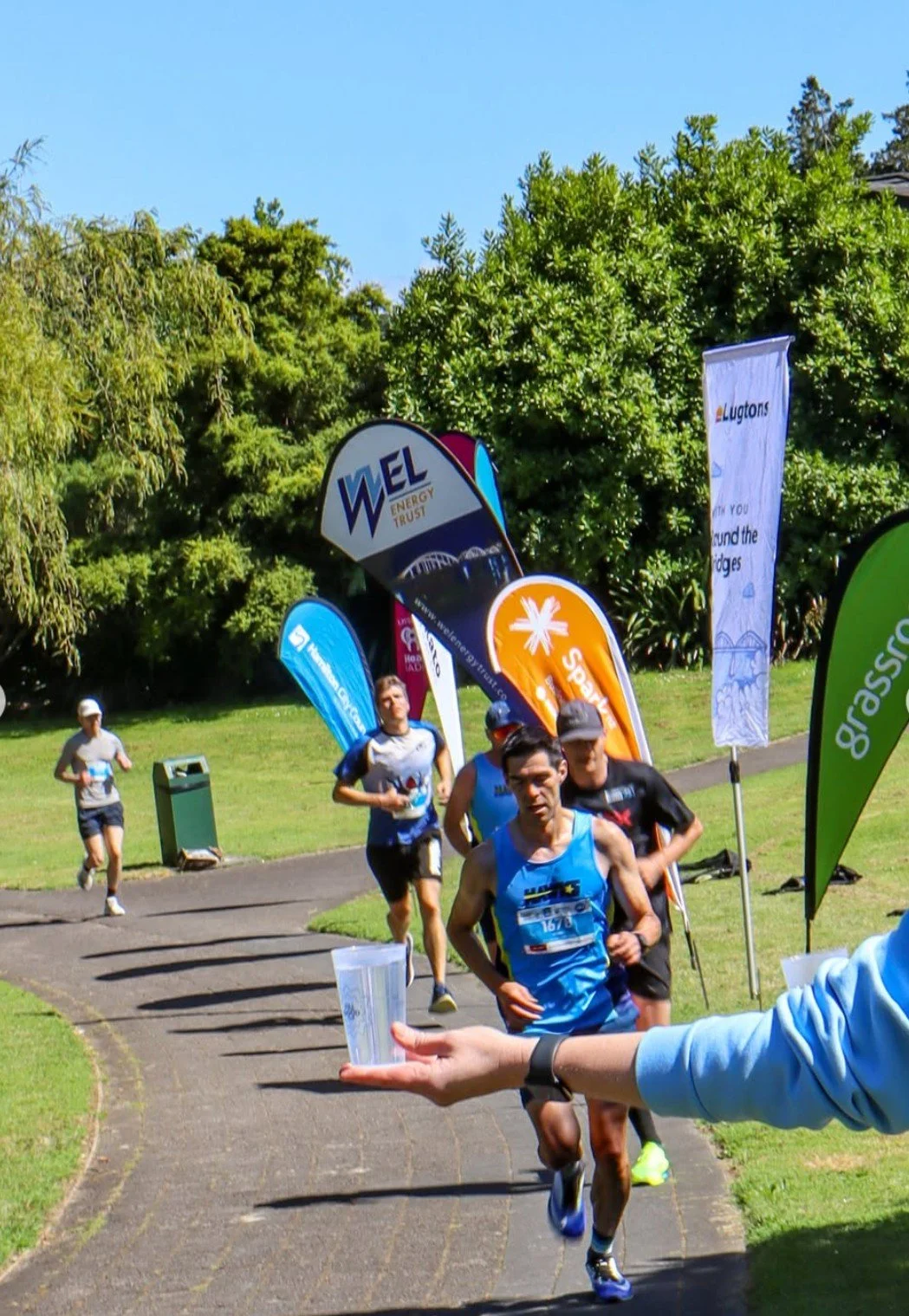 People running round the bridges track in Hamilton with a reusable fillgood cup waiting for them to drink