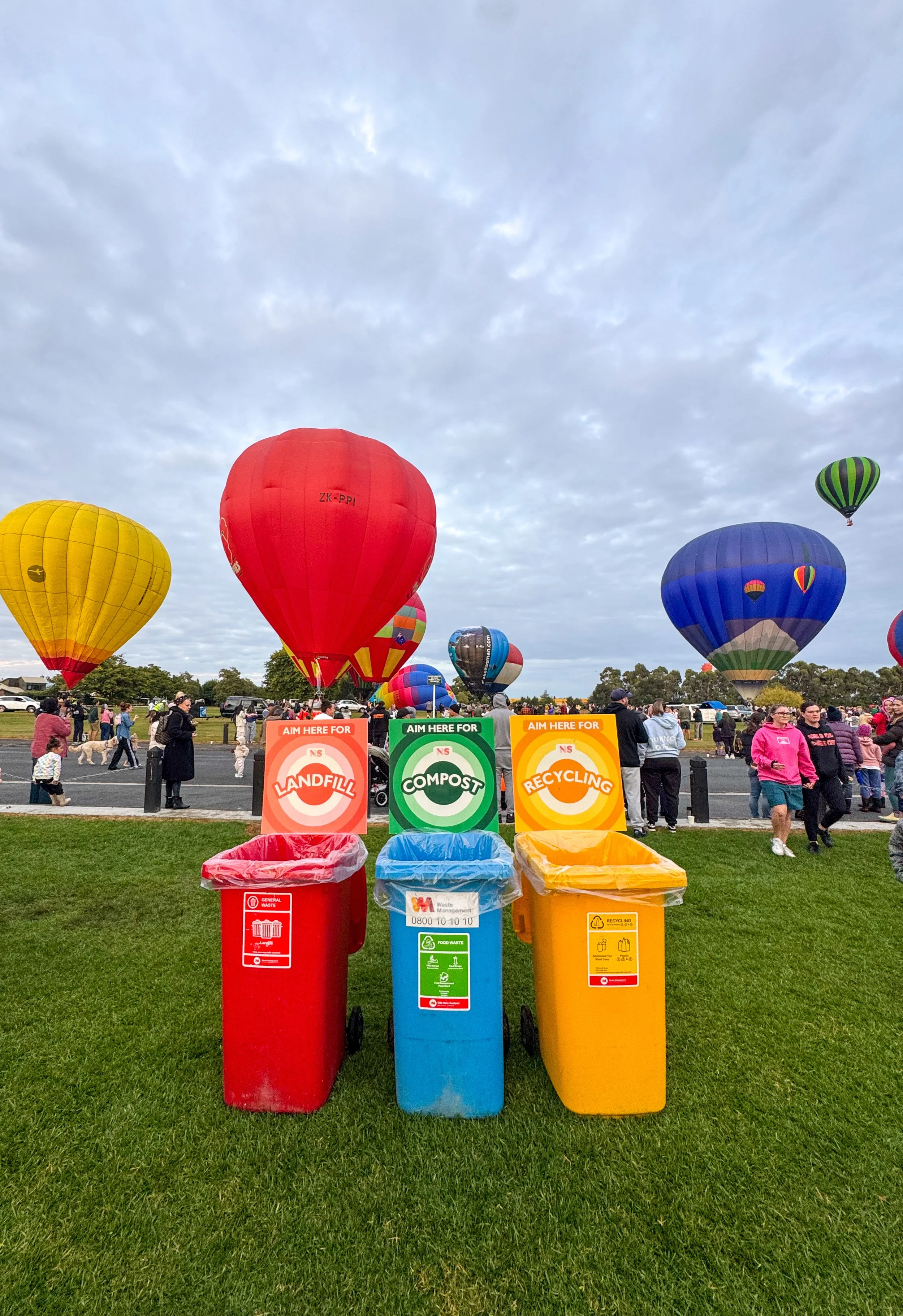 Landfill, compost, and recycling bins at balloons over Waikato community event with fun signage and hot air balloons in the background