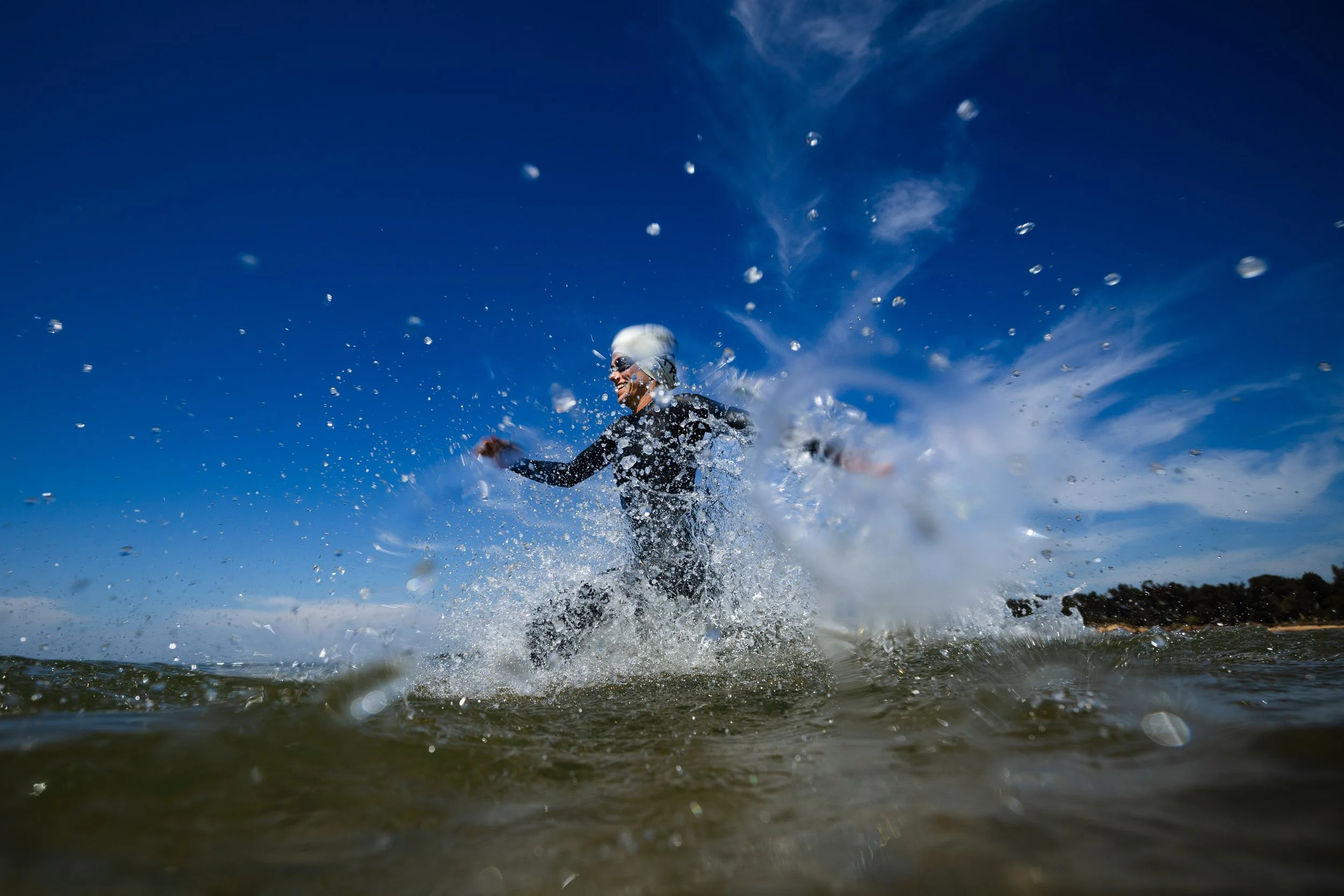 Triathlete running into ocean at race start, captured by Stef Hanson showcasing dynamic sports photography and perfect timing in aquatic conditions.